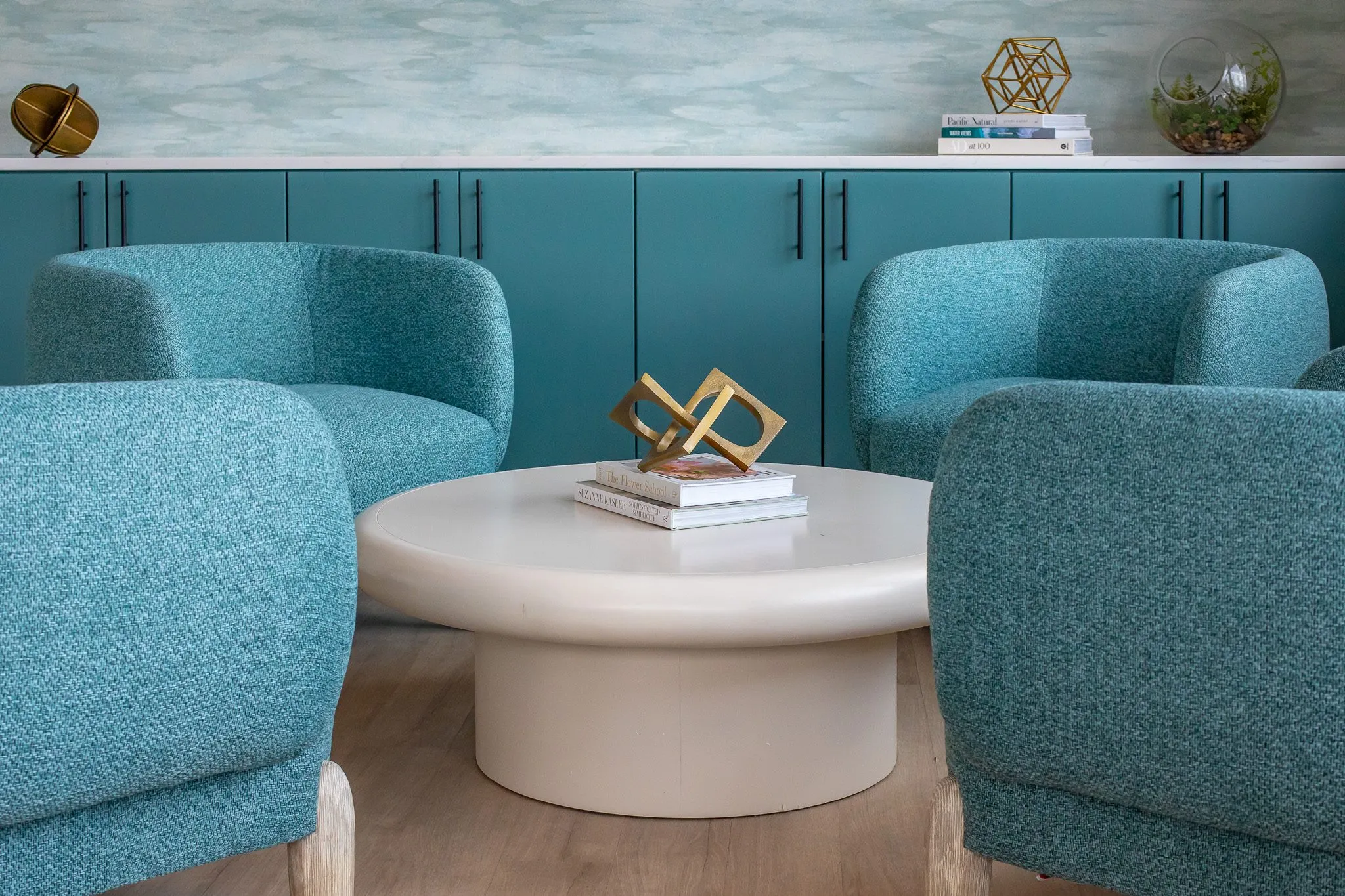 Multifamily interior detail: teal boucle barrel chairs around a white drum table with a brass sculpture before teal cabinets