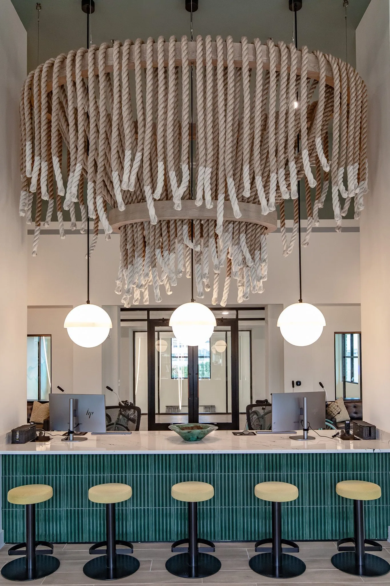 Multifamily leasing desk in fluted teal tile with yellow stools below the full rope chandelier and globe pendants