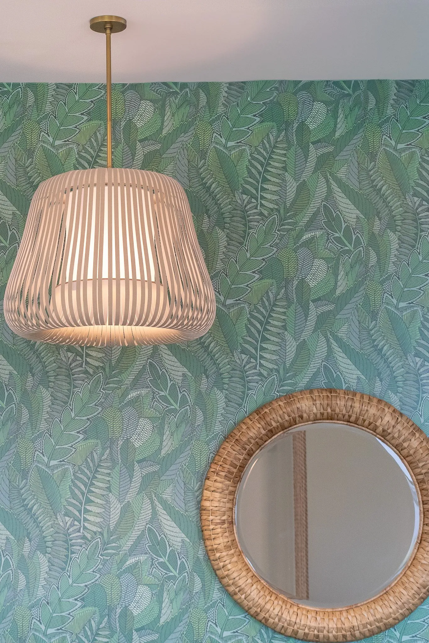 Multifamily interior detail: rattan drum pendant and a round woven mirror against green tropical leaf wallpaper