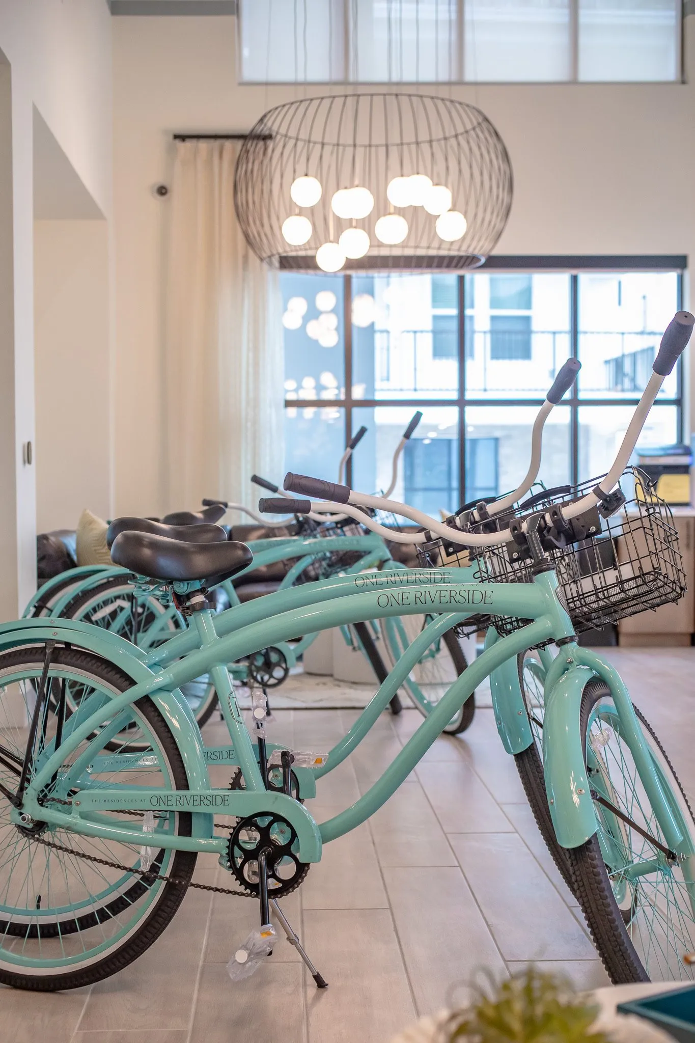 Multifamily amenity bike room with mint cruiser bicycles under a wire cage chandelier with globe bulbs