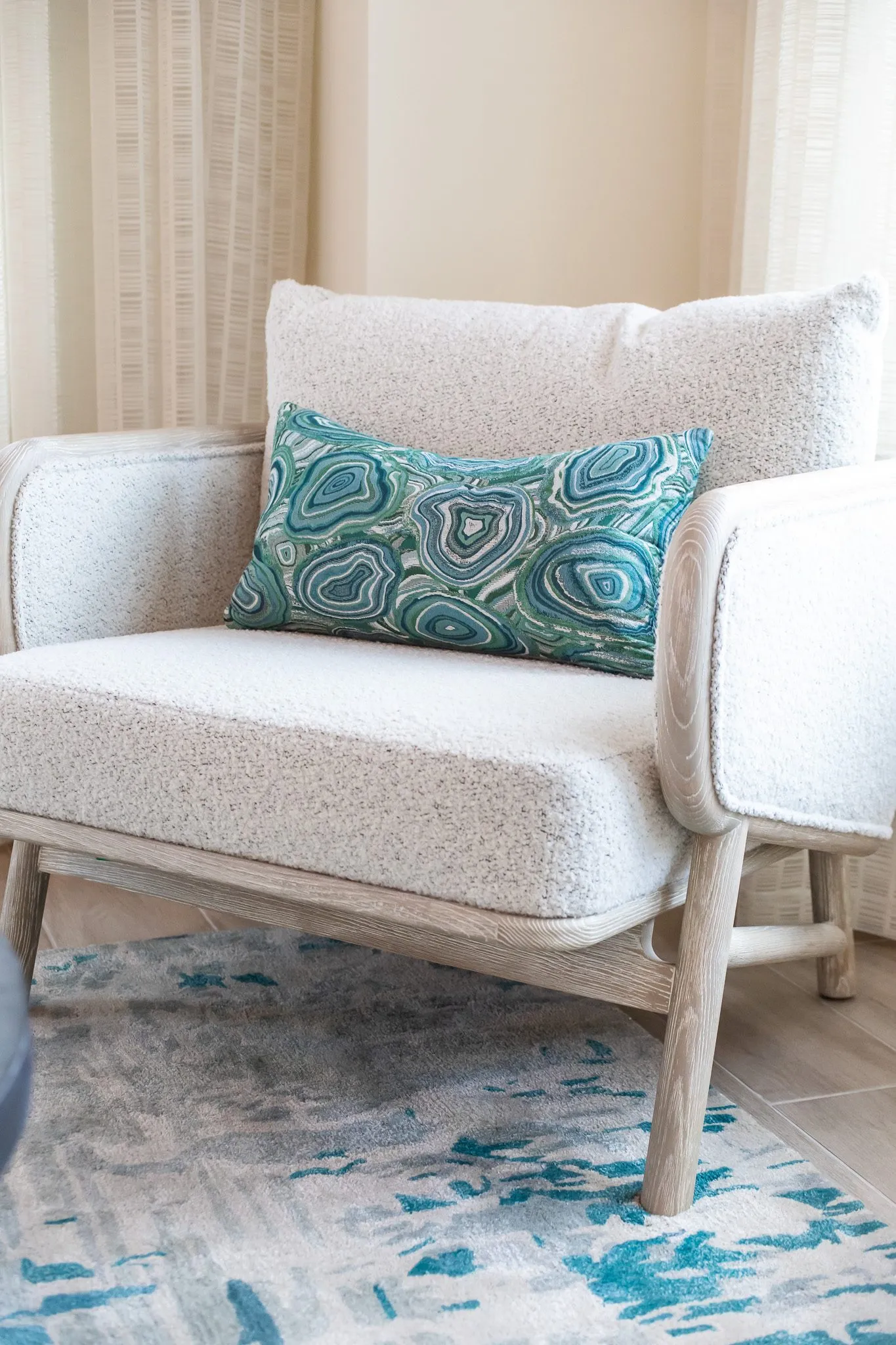 Multifamily interior detail: cream boucle armchair with a teal agate print pillow on a blue and white rug