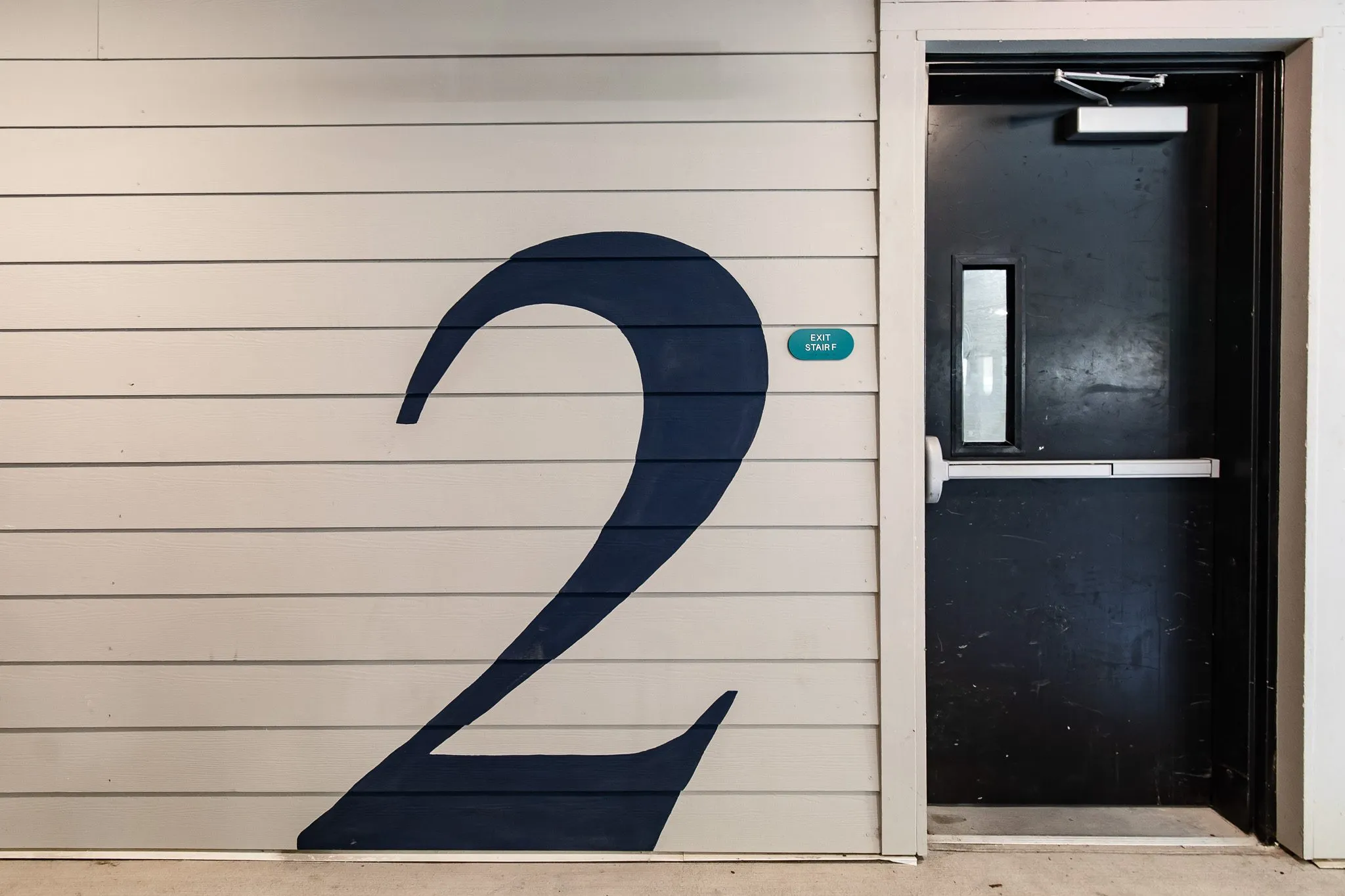 Multifamily interior detail: large navy number 2 painted on white shiplap beside a black stair door
