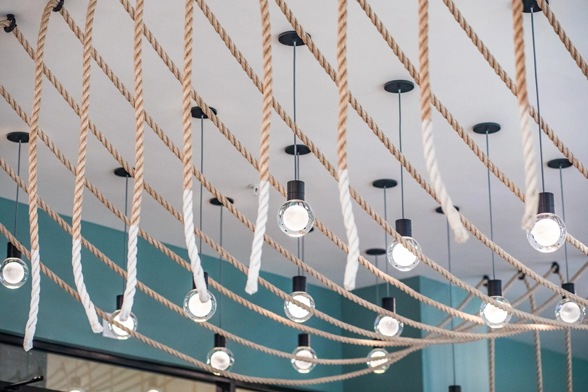 Multifamily interior detail: draped rope strands threaded with bare bulb pendants against a teal wall