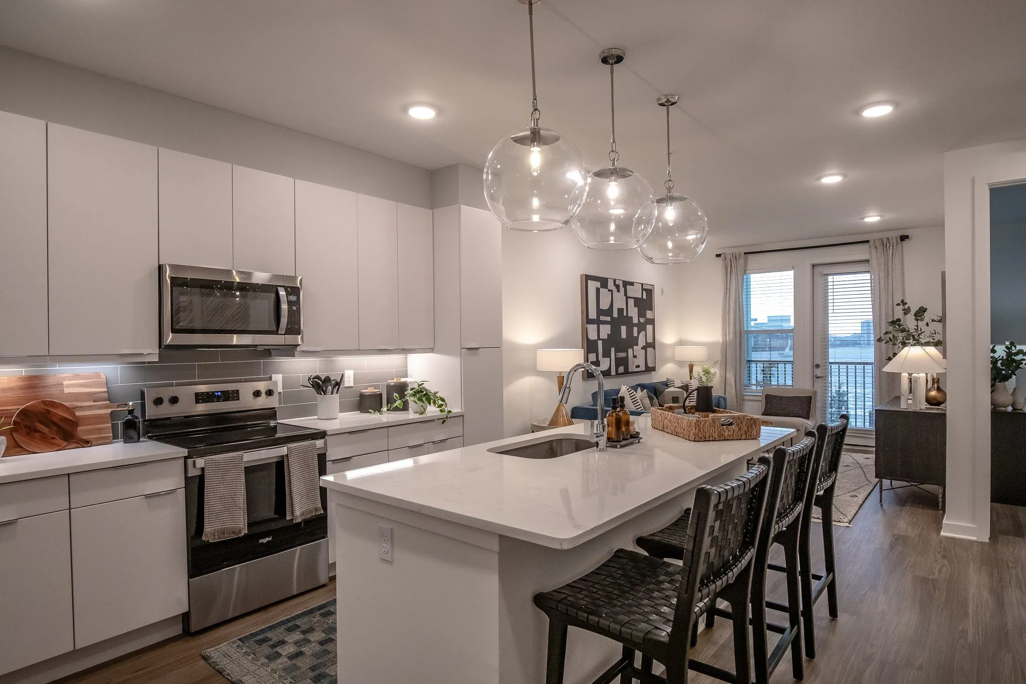 Multifamily model apartment kitchen with white cabinets, a quartz island with woven barstools and glass globe pendants