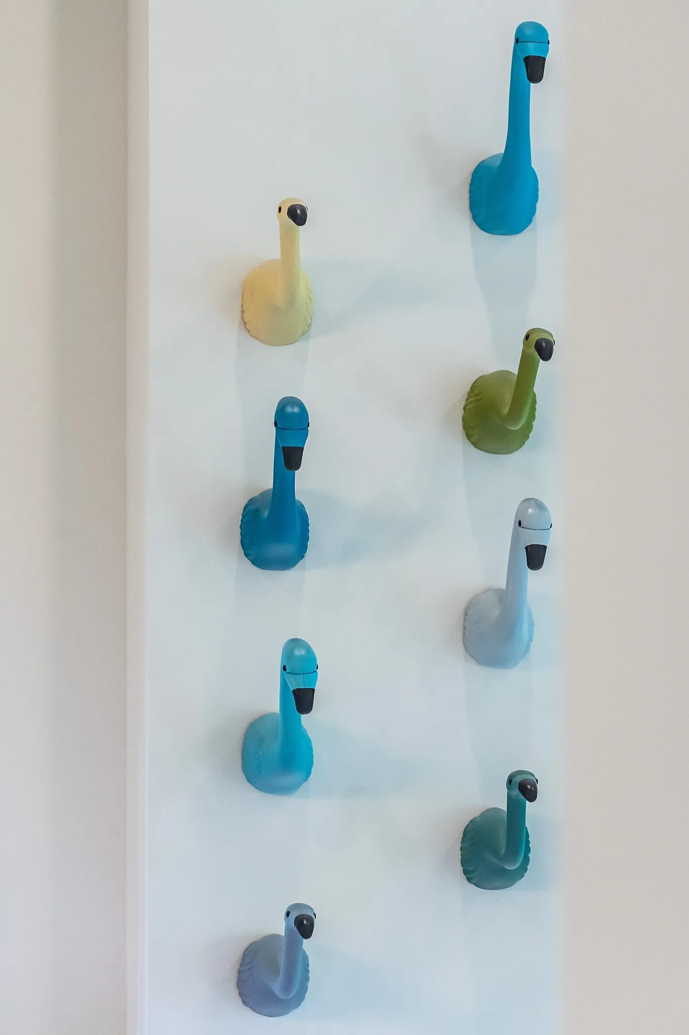 Multifamily interior detail: wall of ceramic flamingo head hooks in yellow, blues and greens in two columns