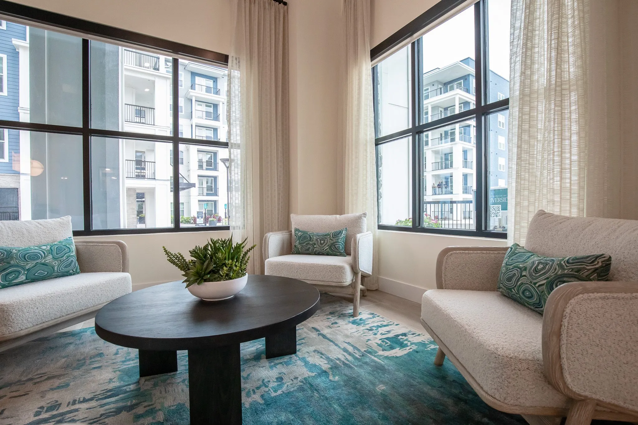 Multifamily model apartment living room with cream boucle chairs and settee around a black table on a teal rug