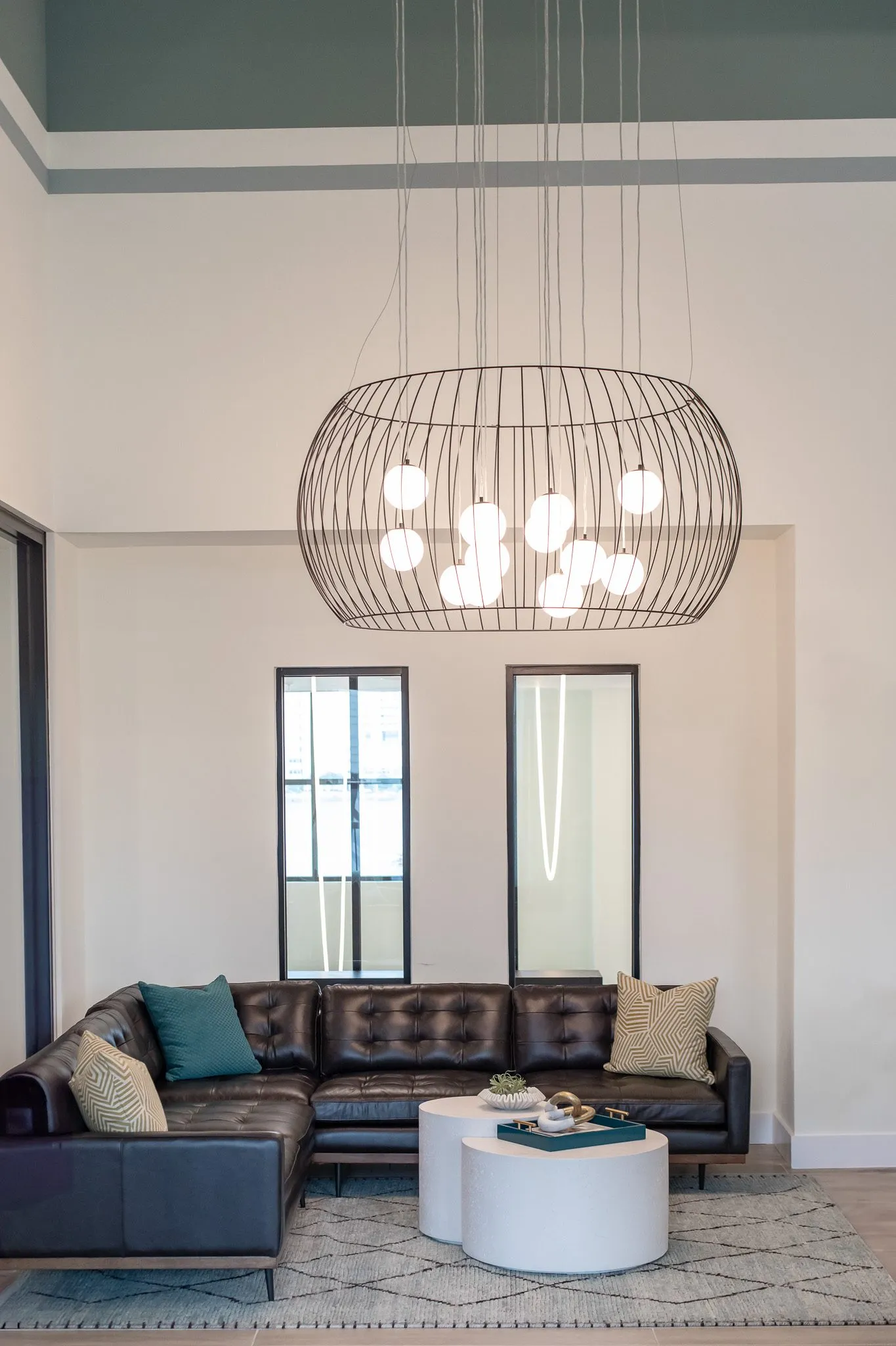 Multifamily amenity lounge with a wire cage chandelier of globe bulbs high above a black leather sectional and two windows