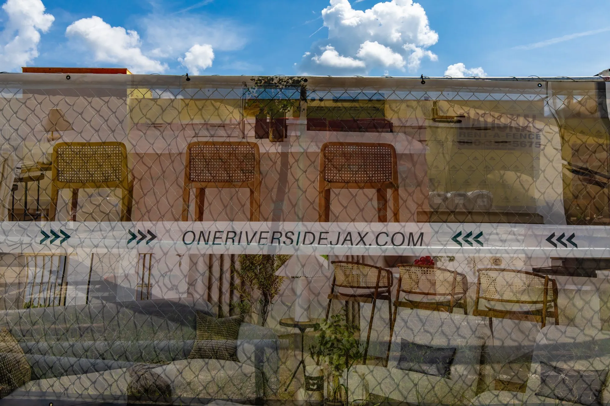 Multifamily community under construction: chain link fence with a banner of rendered seating and green chevrons