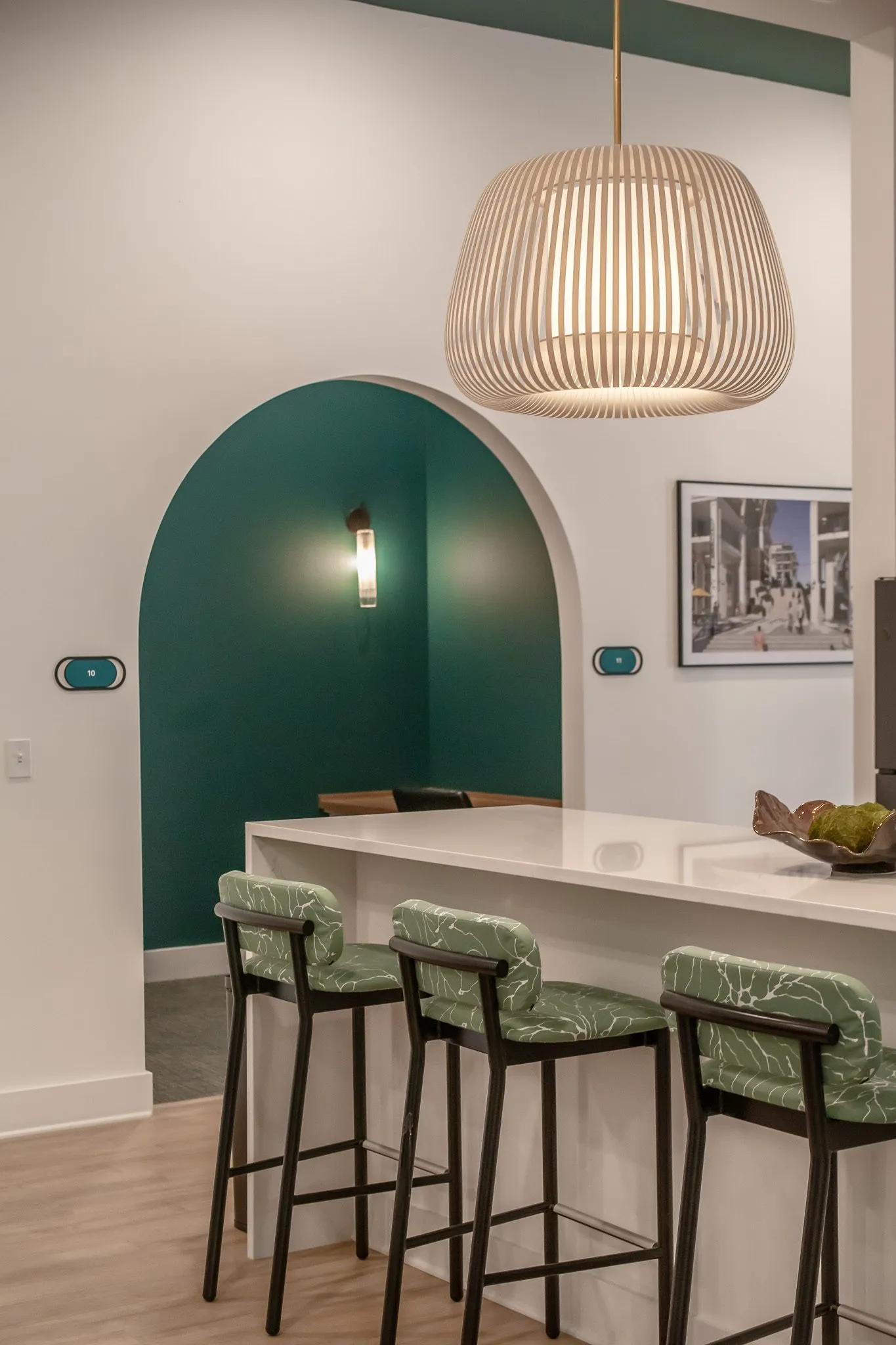 Multifamily interior detail: leaf print barstools at a white counter below a slatted pendant, a teal arched niche behind