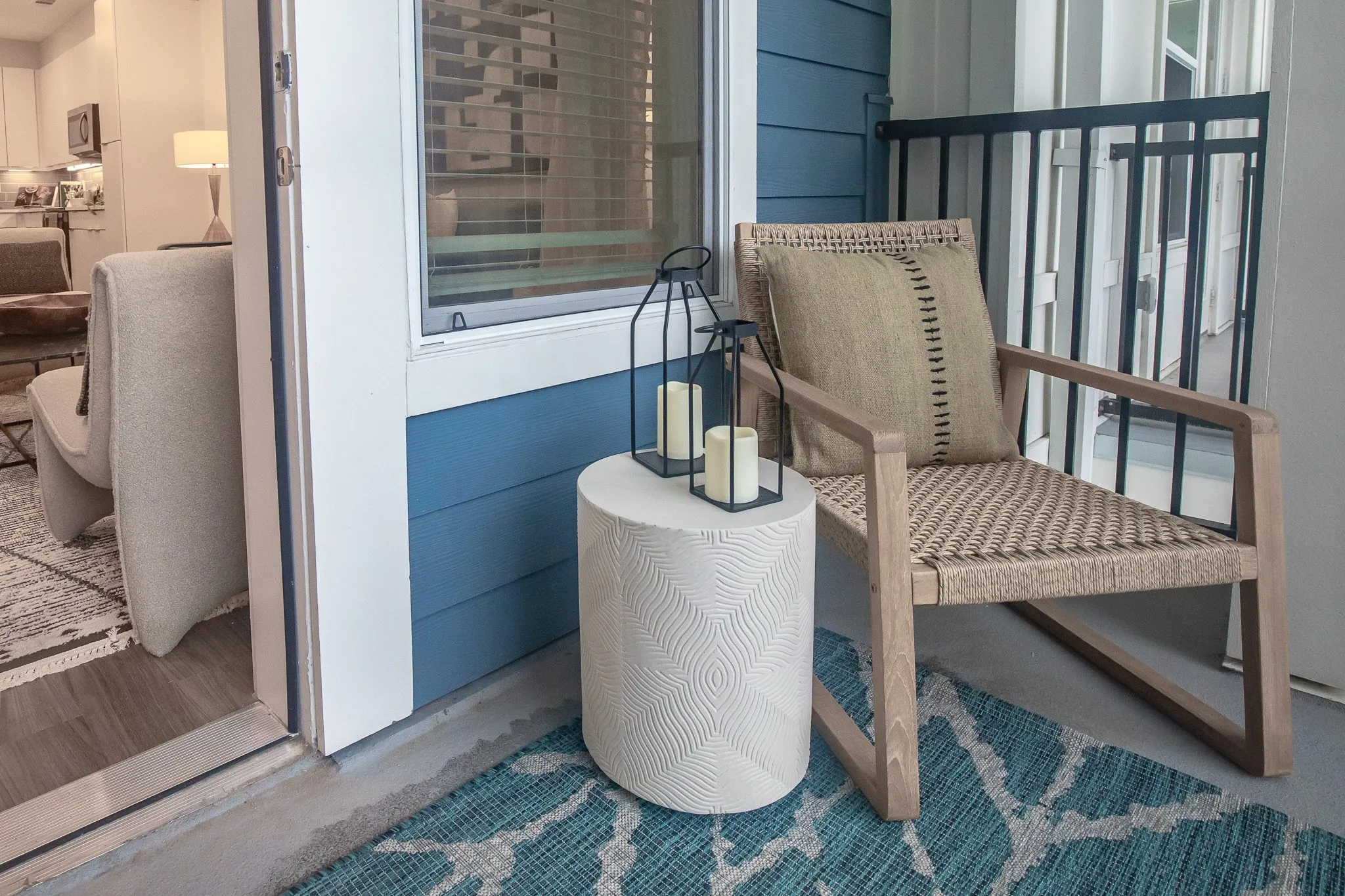 Multifamily apartment balcony with a woven rope armchair, white ceramic side table and lantern on a teal patterned rug