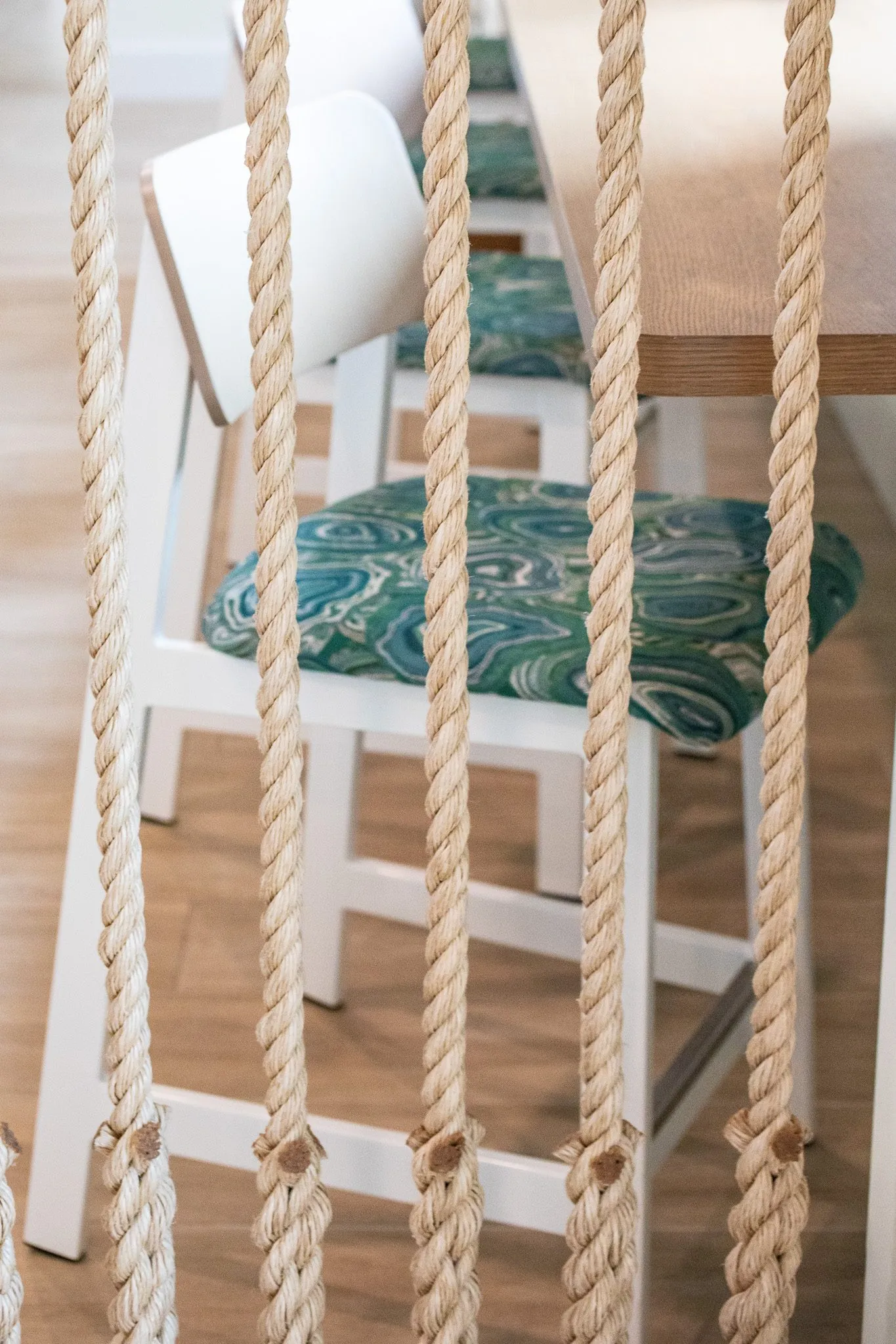 Multifamily interior detail: through rope strands to white chairs with green agate print seats at a wood counter