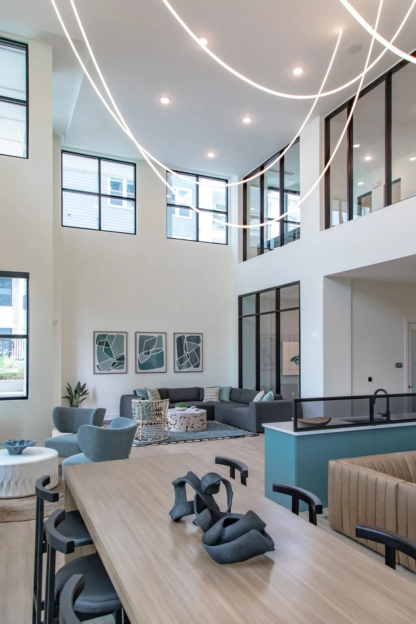 Multifamily amenity two storey lounge from a communal table with a sculpture, sectional and looping light above
