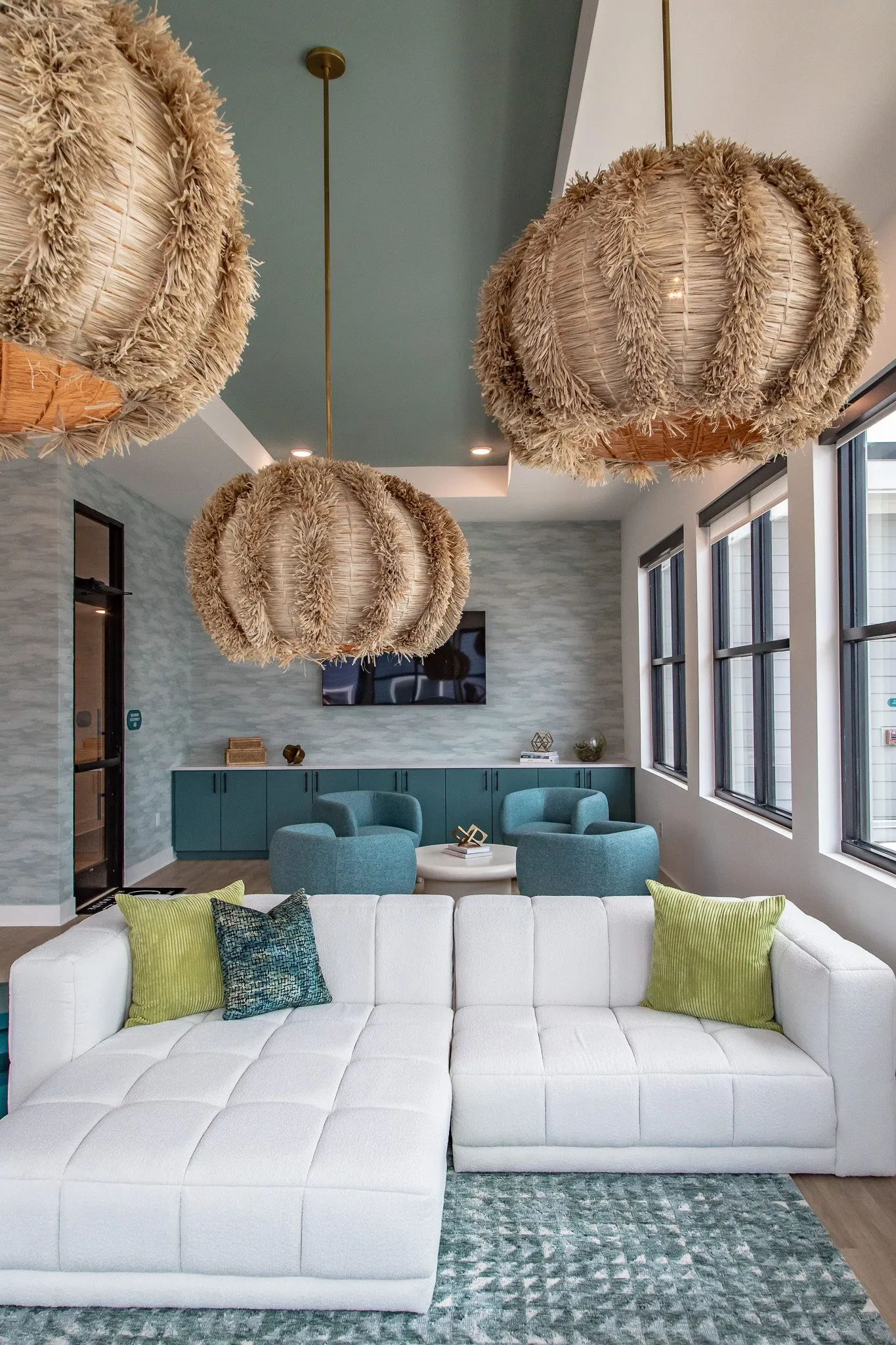 Multifamily amenity lounge under fringed rattan pendants, a white sectional before teal chairs and cabinets