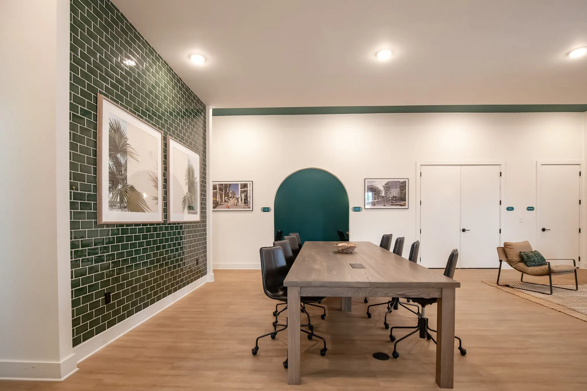 Multifamily amenity conference room from the corner, green tile wall with palm prints, a lounge chair and teal arch behind