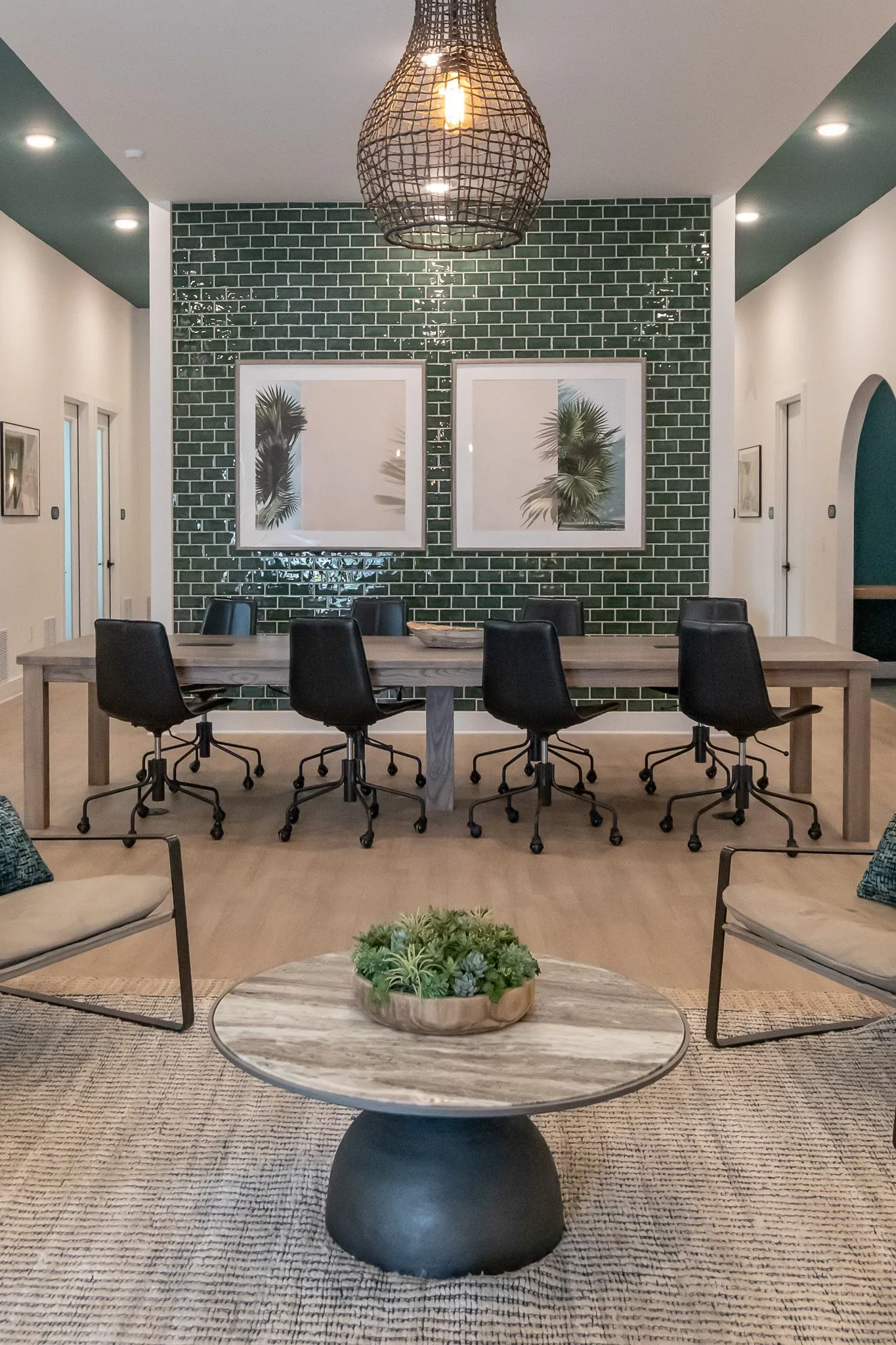 Multifamily amenity lounge with a round table and woven pendant before the conference table and green tile wall