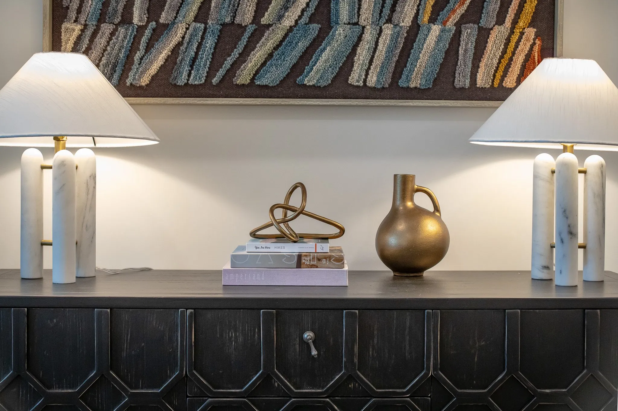 Multifamily interior detail: black carved sideboard with marble column lamps, a brass vase and knot sculpture