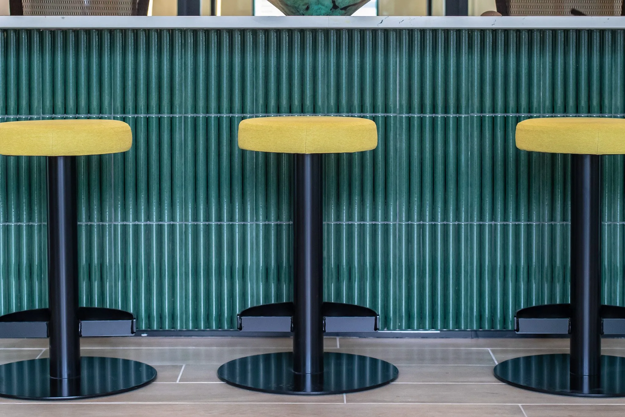 Multifamily interior detail: yellow topped stools on black pedestals before fluted green tile