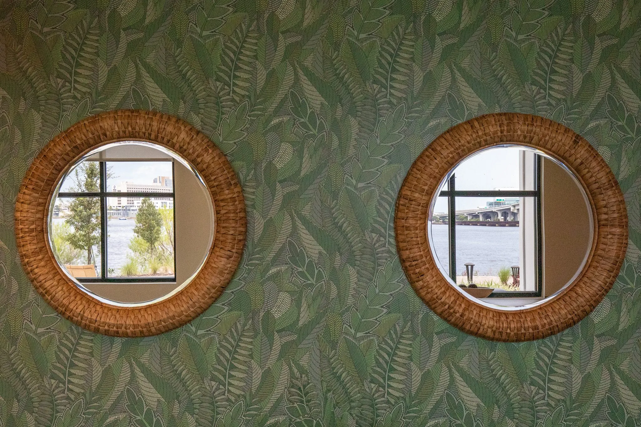 Multifamily interior detail: two round rattan mirrors on green leaf wallpaper reflecting windows onto the water