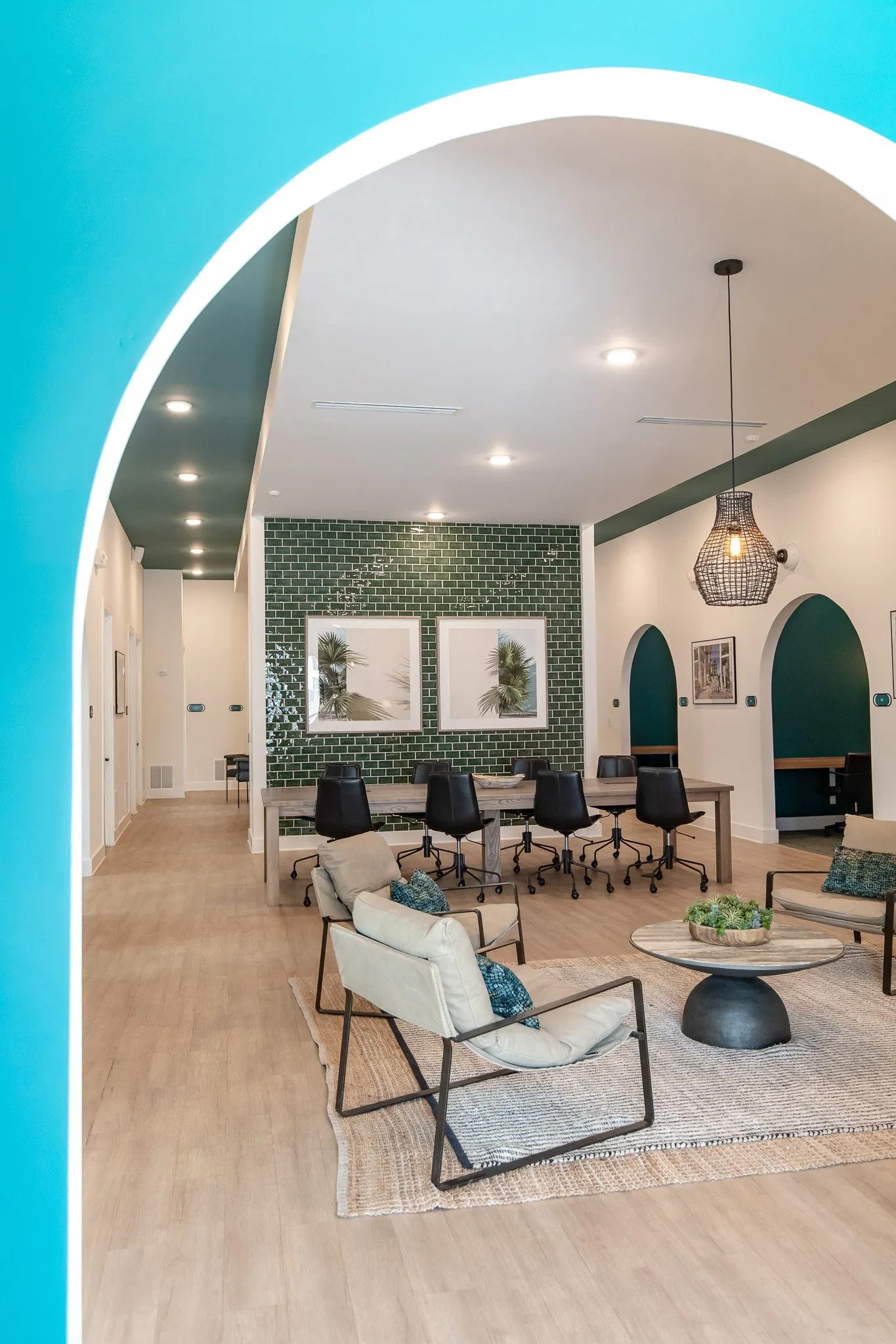 Multifamily amenity lounge seen through a teal arch, a sling chair and round table, conference table and green tile beyond