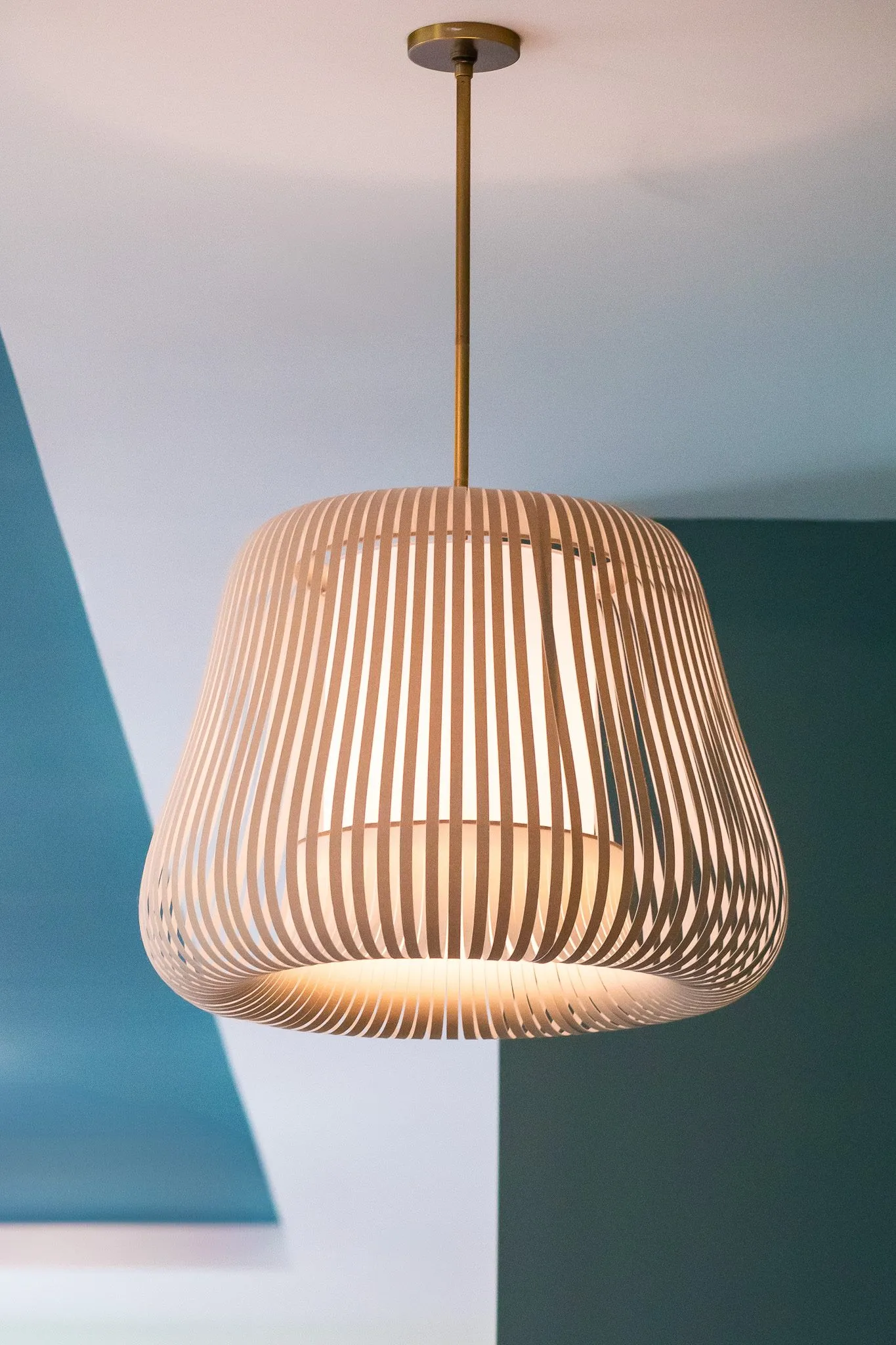 Multifamily interior detail: slatted pale wood pendant with a flared shade against teal and white walls
