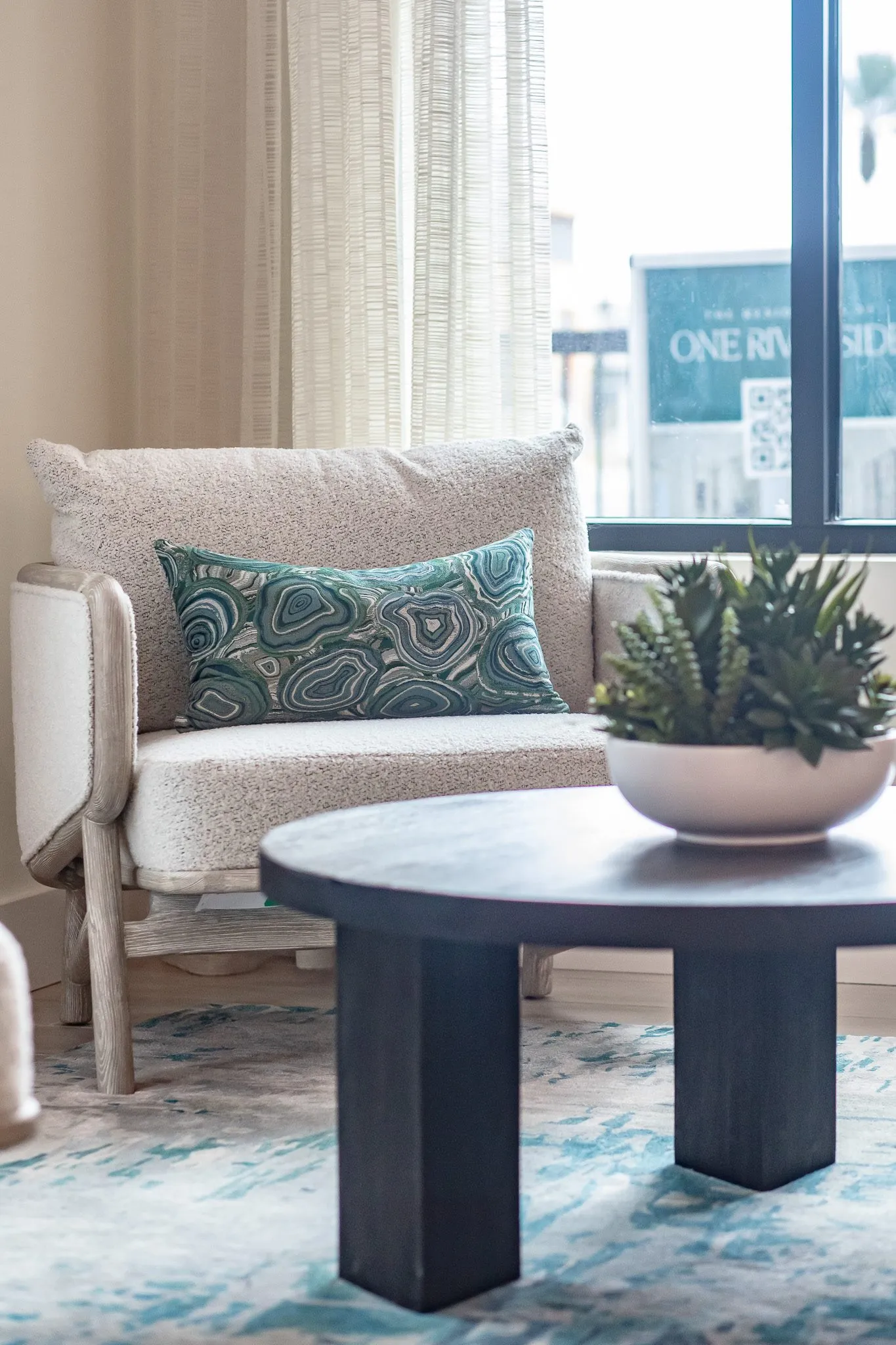 Multifamily interior detail: cream boucle armchair with an agate pillow and a black coffee table with succulents by a window
