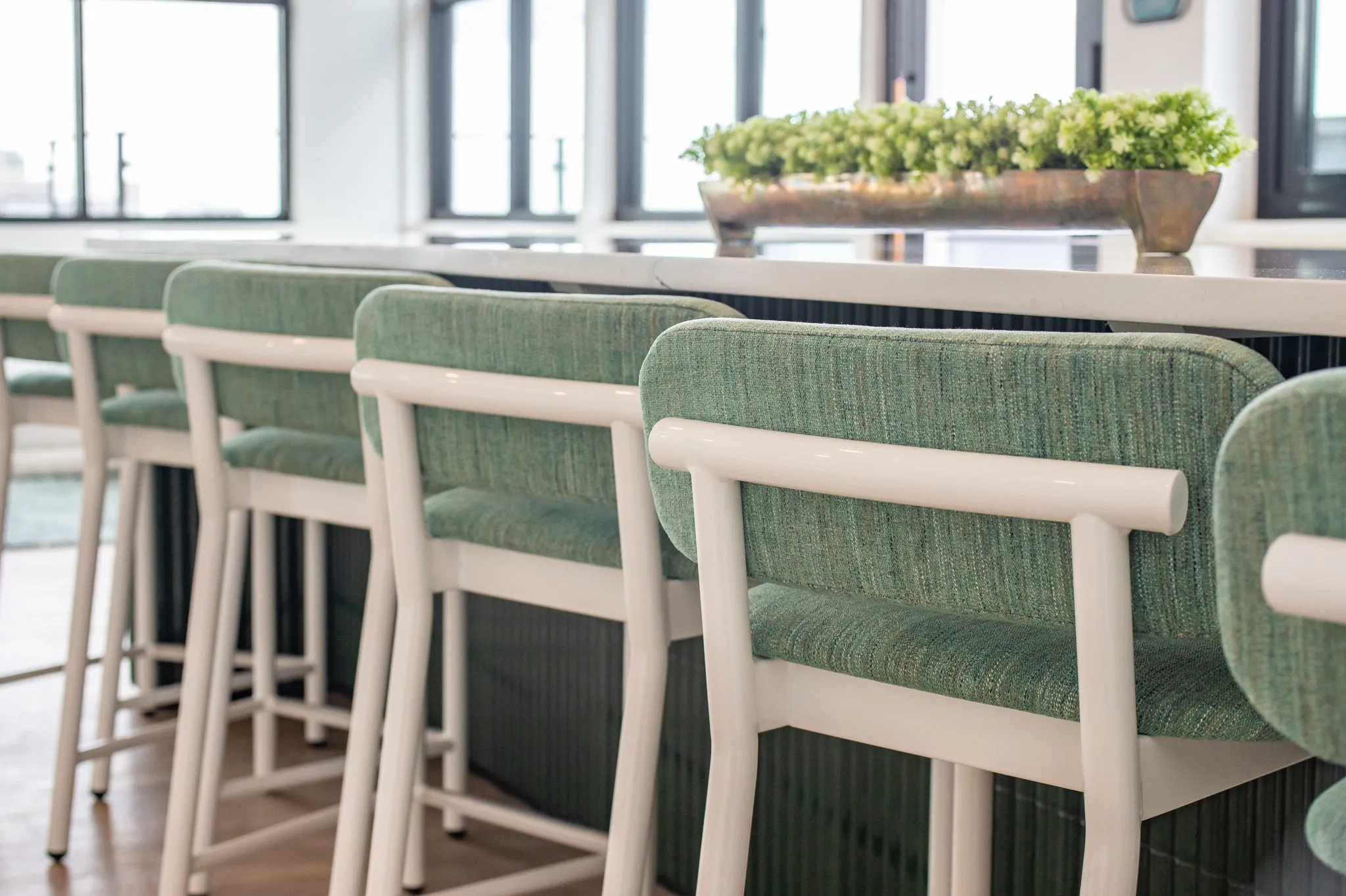 Multifamily interior detail: green upholstered barstools with white frames along a counter with a planter