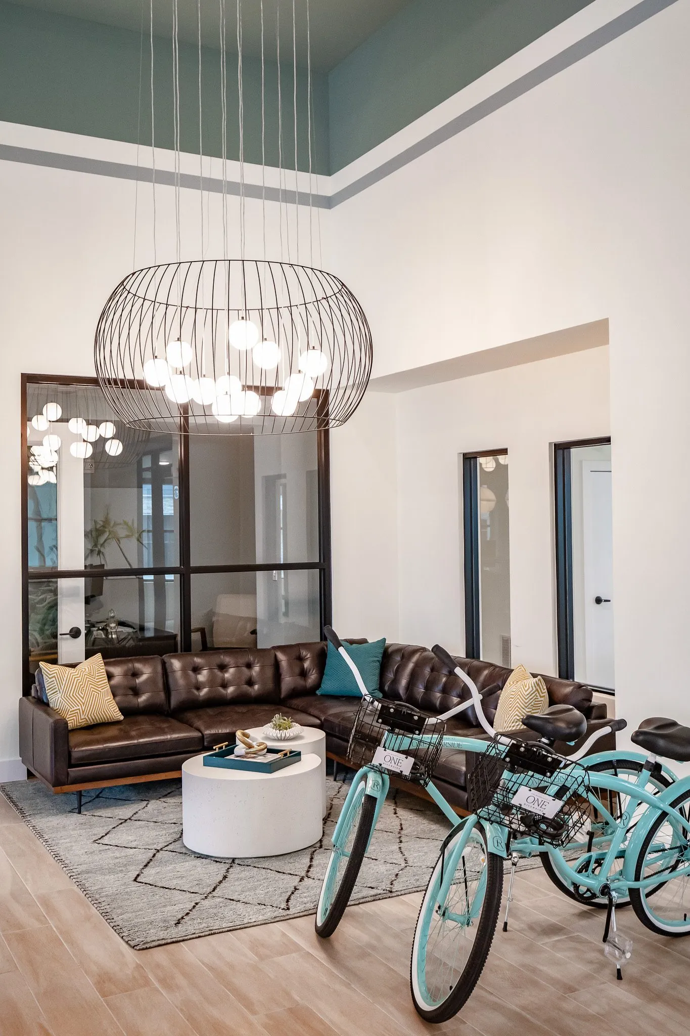 Multifamily amenity bike area: mint bicycles parked before a brown leather sectional under a wire cage chandelier
