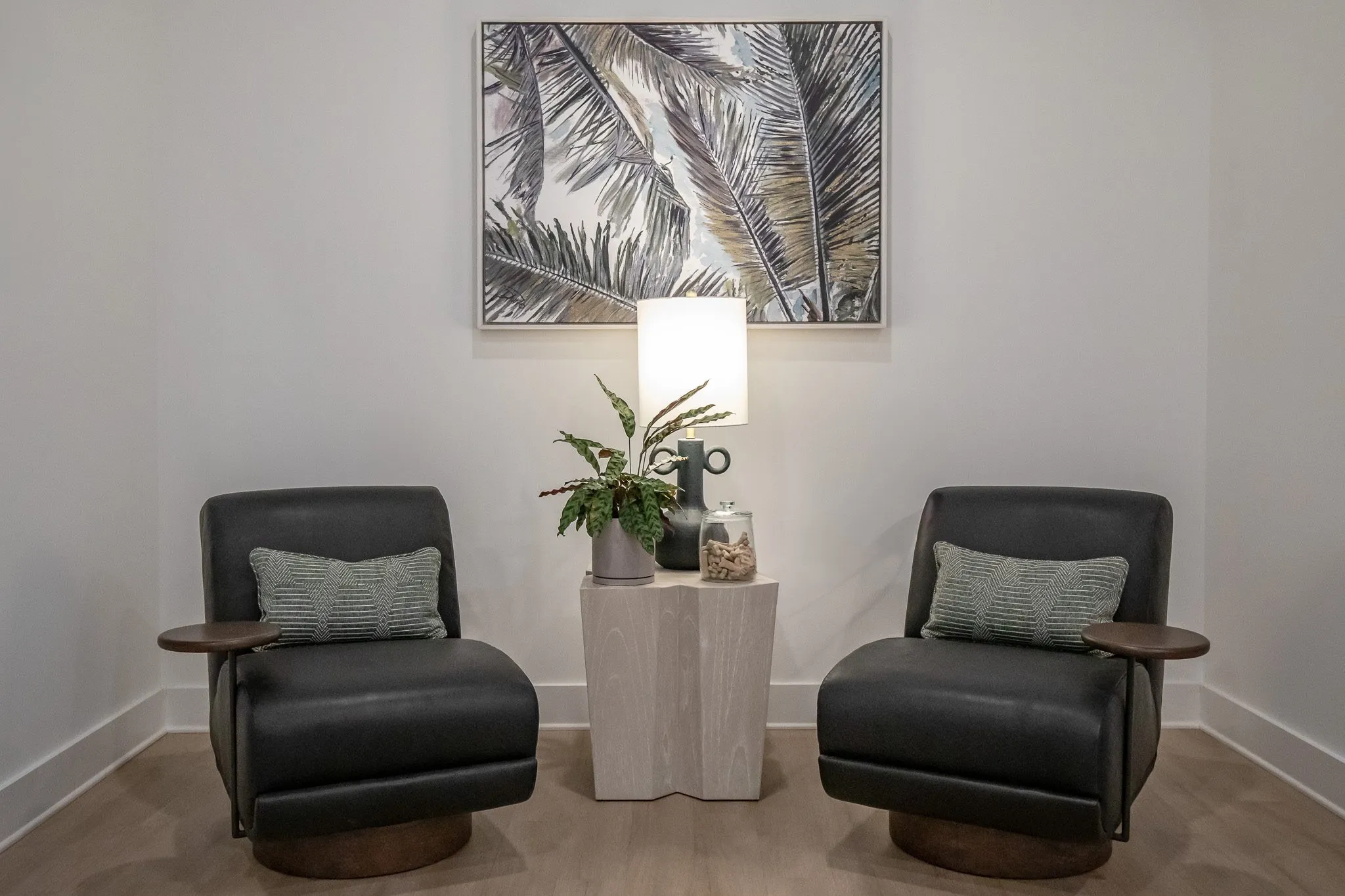 Multifamily interior detail: two charcoal leather swivel chairs flanking a stone pedestal table below a palm frond print