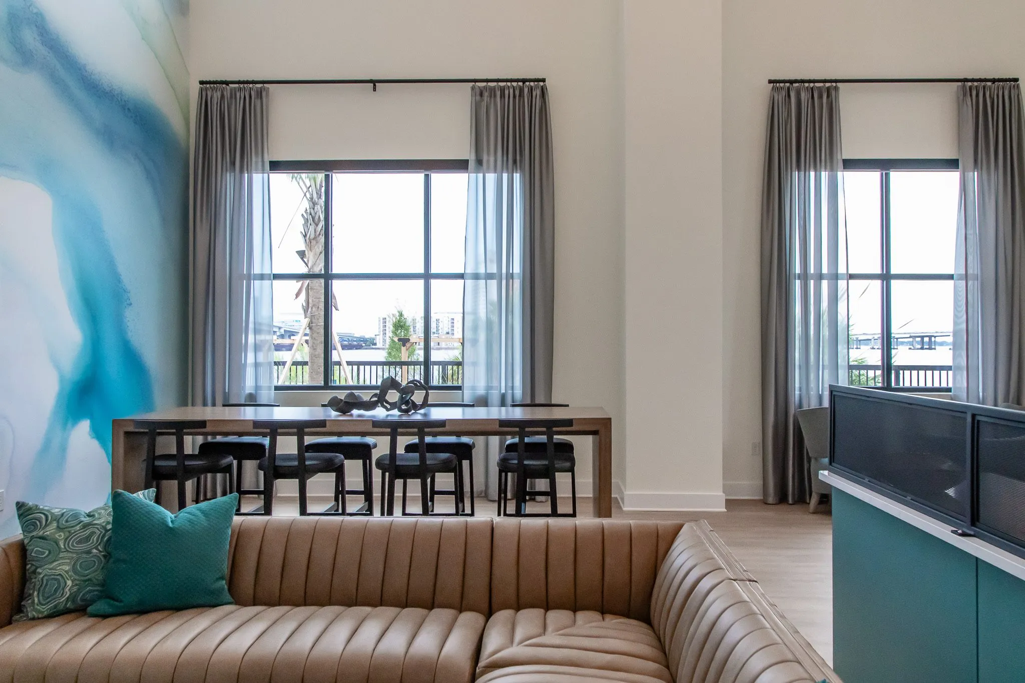 Multifamily amenity lounge with a tan channelled sofa and teal pillows before a communal table with black stools