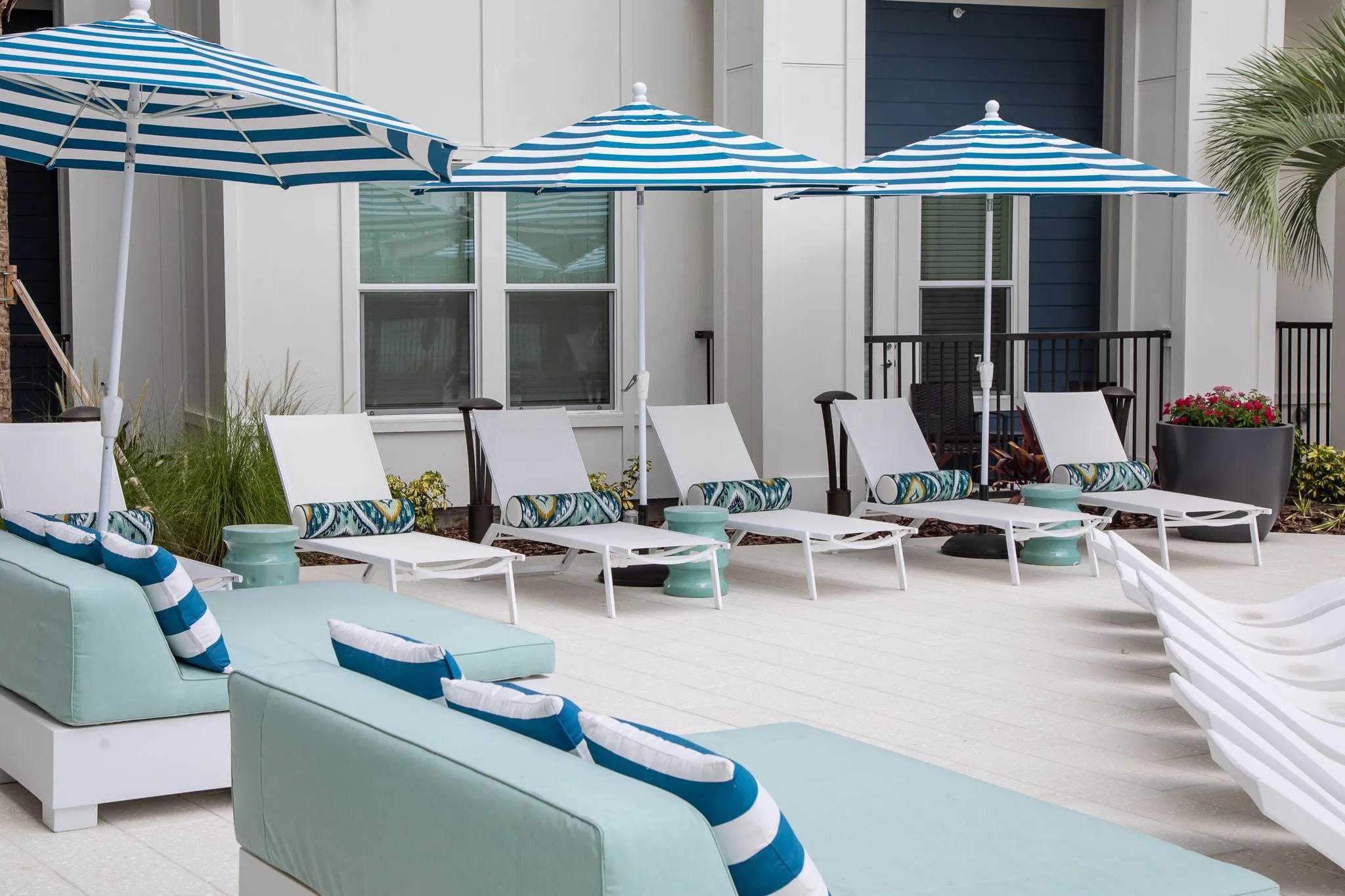 Multifamily amenity pool deck with mint cushioned lounge seating and white chaises under blue and white umbrellas