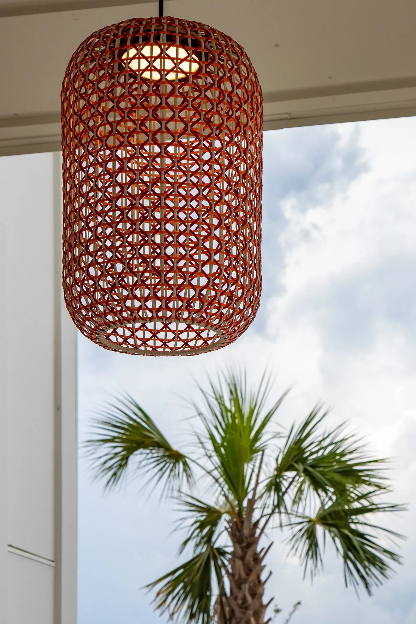 Multifamily community exterior: red woven cylinder pendant under a porch soffit with a palm tree beyond