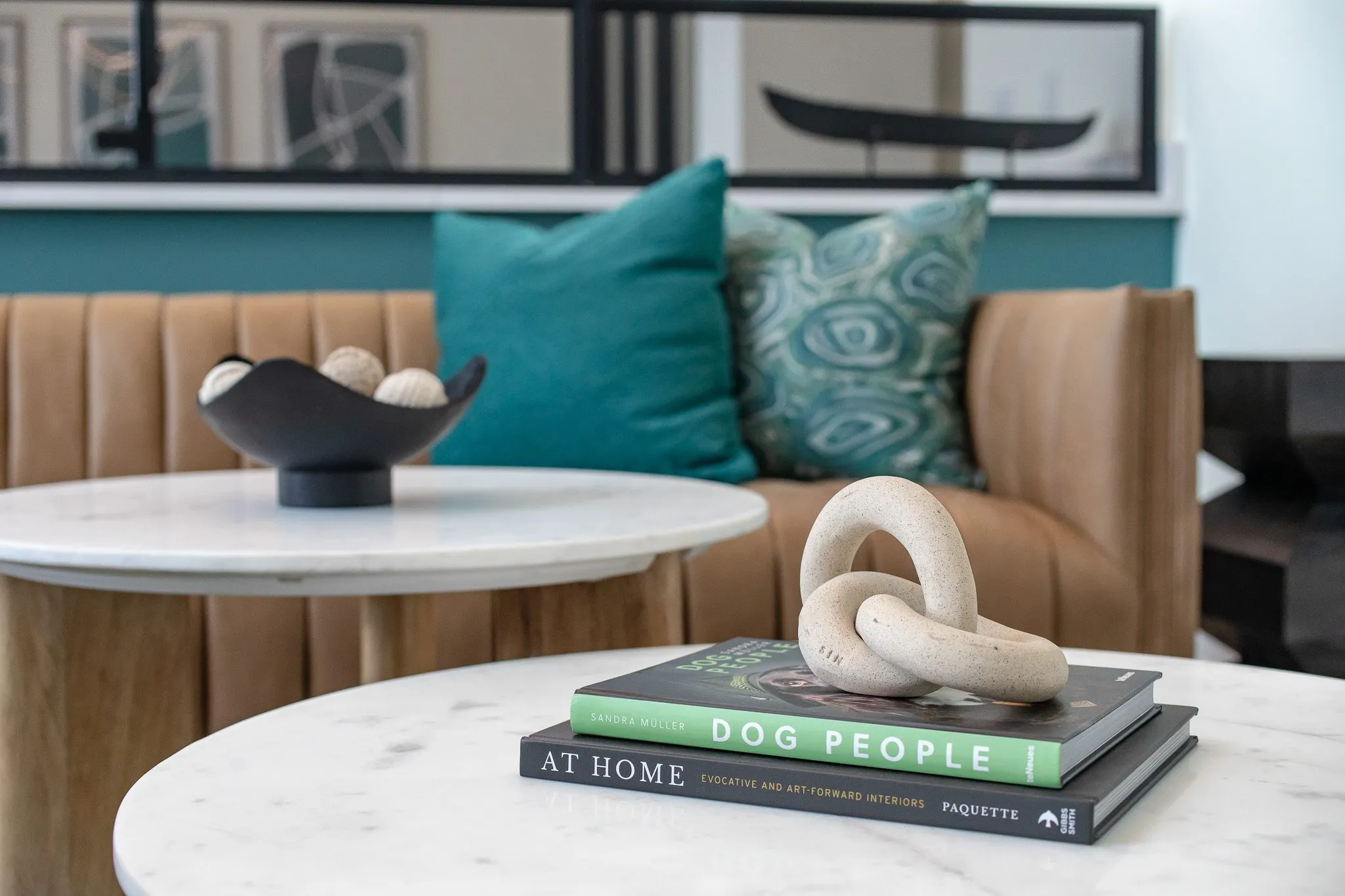 Multifamily interior detail: stone link sculpture on books atop a marble table, a tan banquette with teal pillows behind