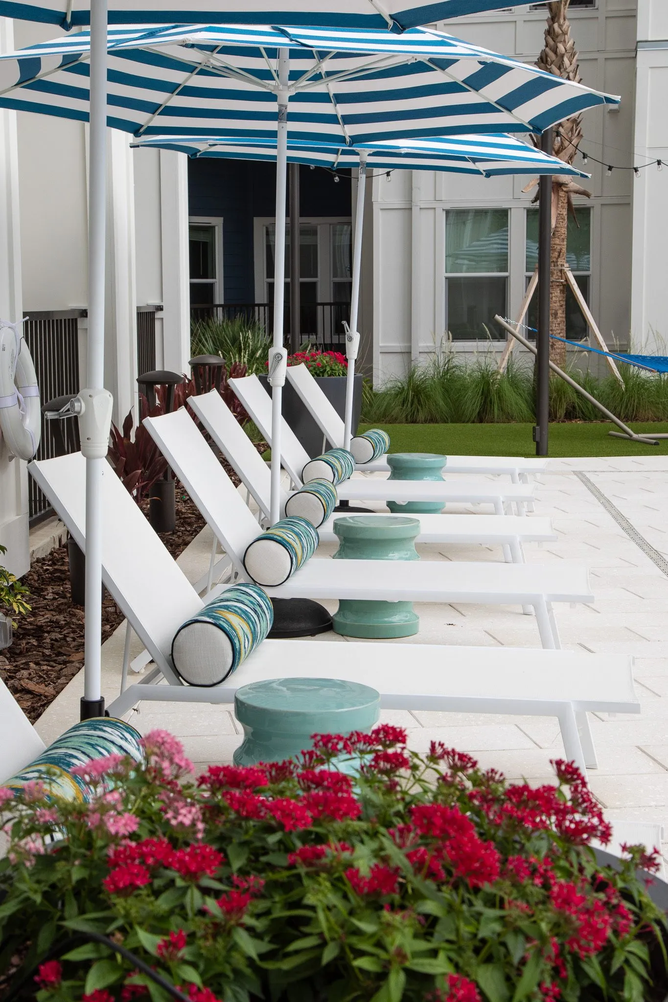 Multifamily amenity chaise loungers with patterned bolsters under striped umbrellas, red flowers in front