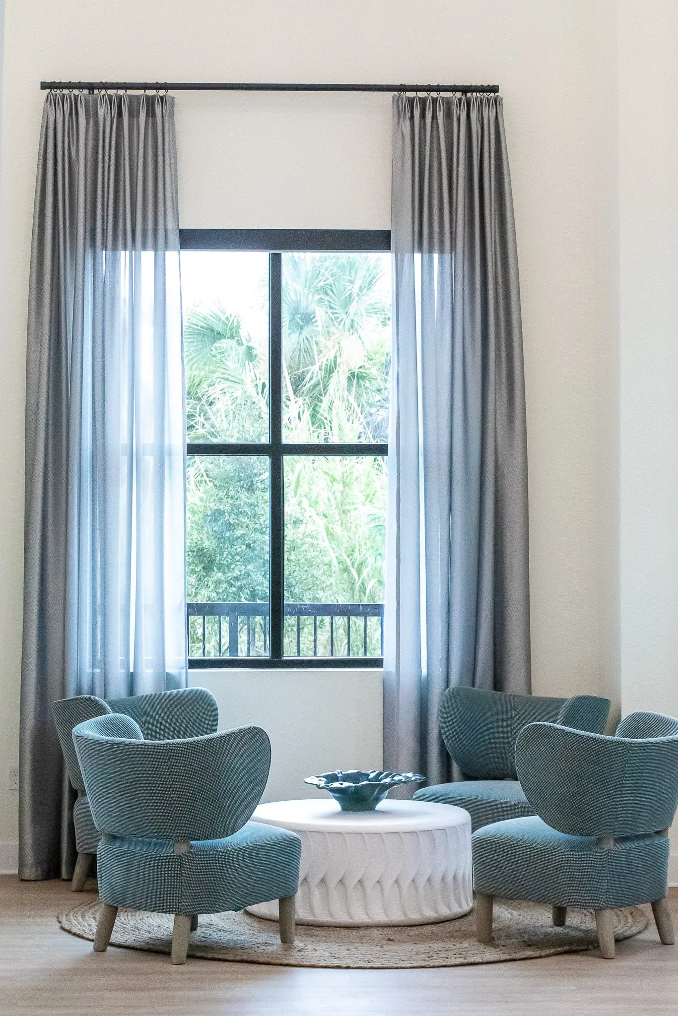 Multifamily amenity lounge with teal boucle chairs around a white fluted drum table on a jute rug by a curtained window