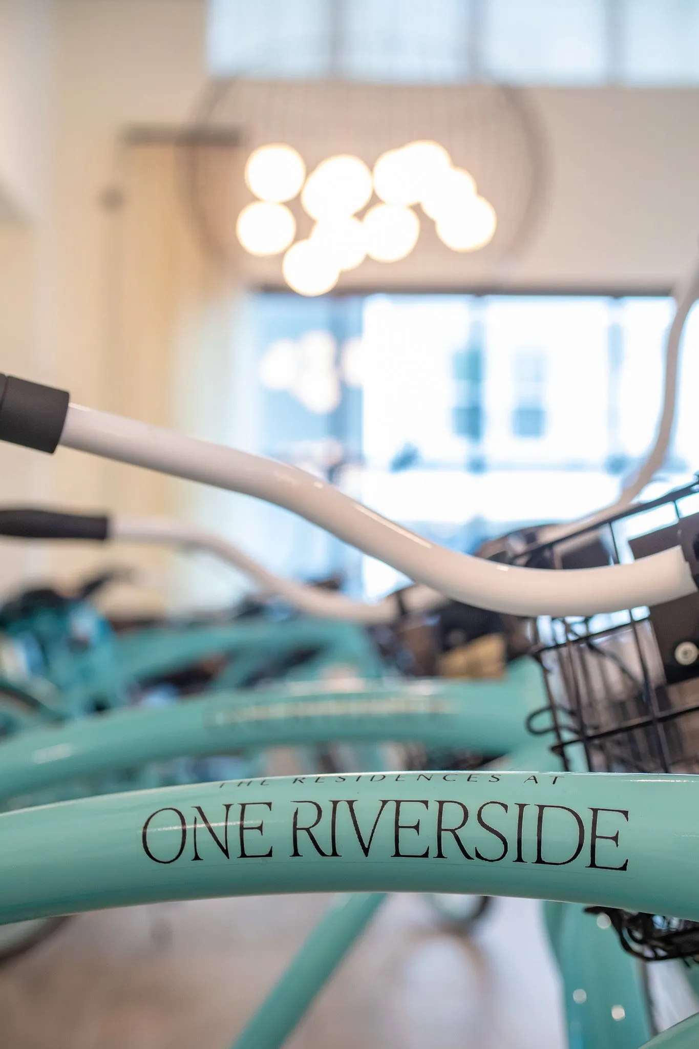 Multifamily interior detail: mint cruiser bicycle with lettering on the frame, a globe chandelier blurred behind