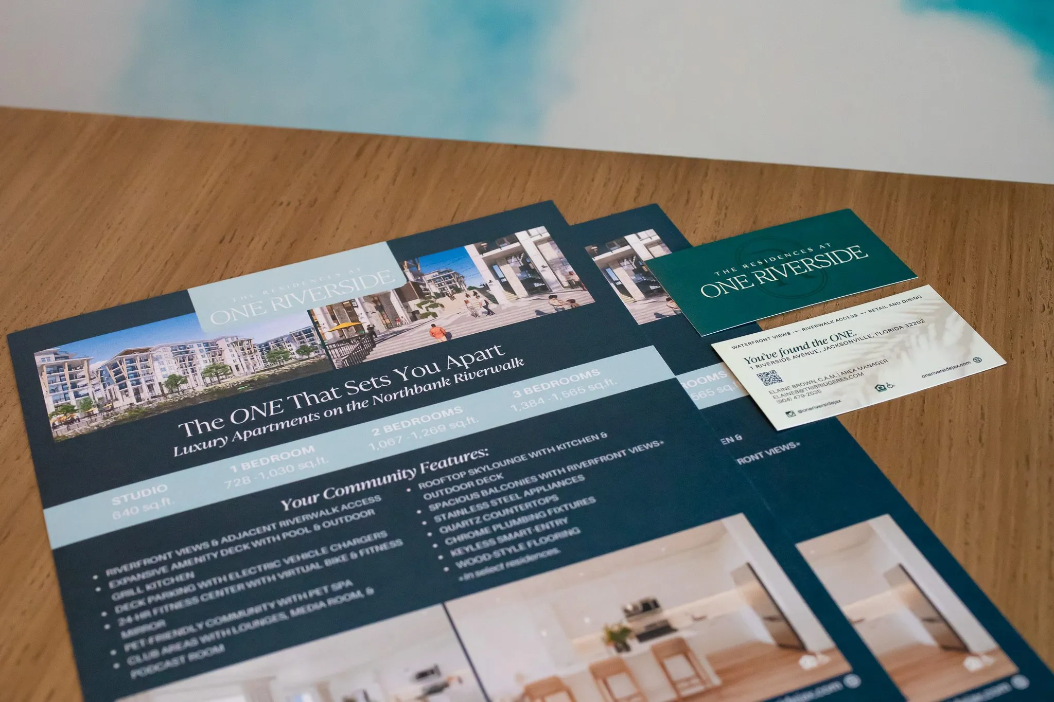 Multifamily leasing collateral: printed flyers and a business card on a wood table
