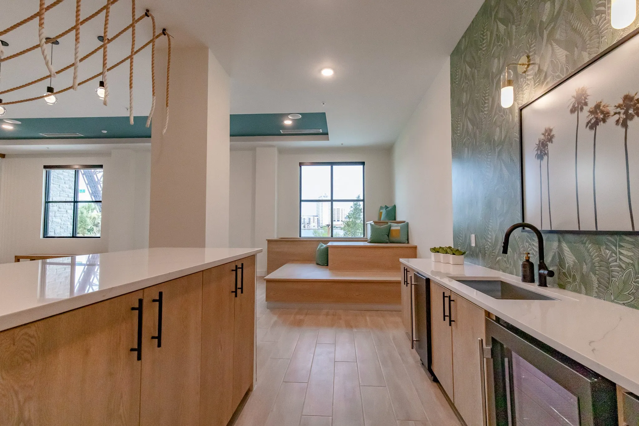 Multifamily amenity kitchenette with wood cabinets and a white island before palm print art on leaf wallpaper
