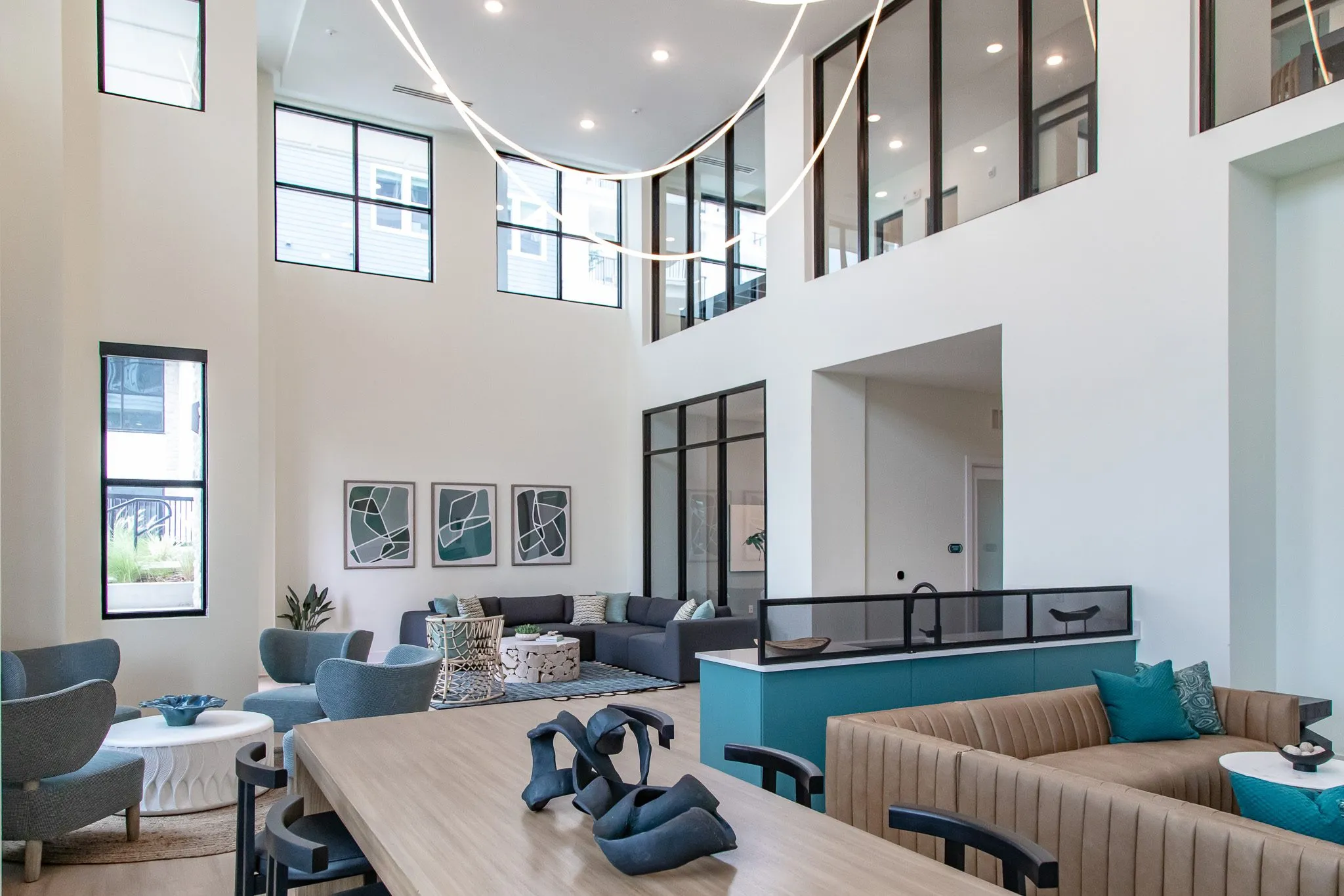 Multifamily amenity two storey lounge with a communal table and black sculpture, tan banquette and teal counter