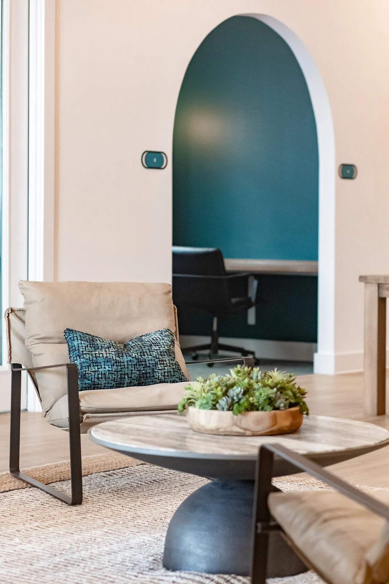 Multifamily interior detail: leather sling chair and a marble table with succulents, a teal arched niche with a desk chair
