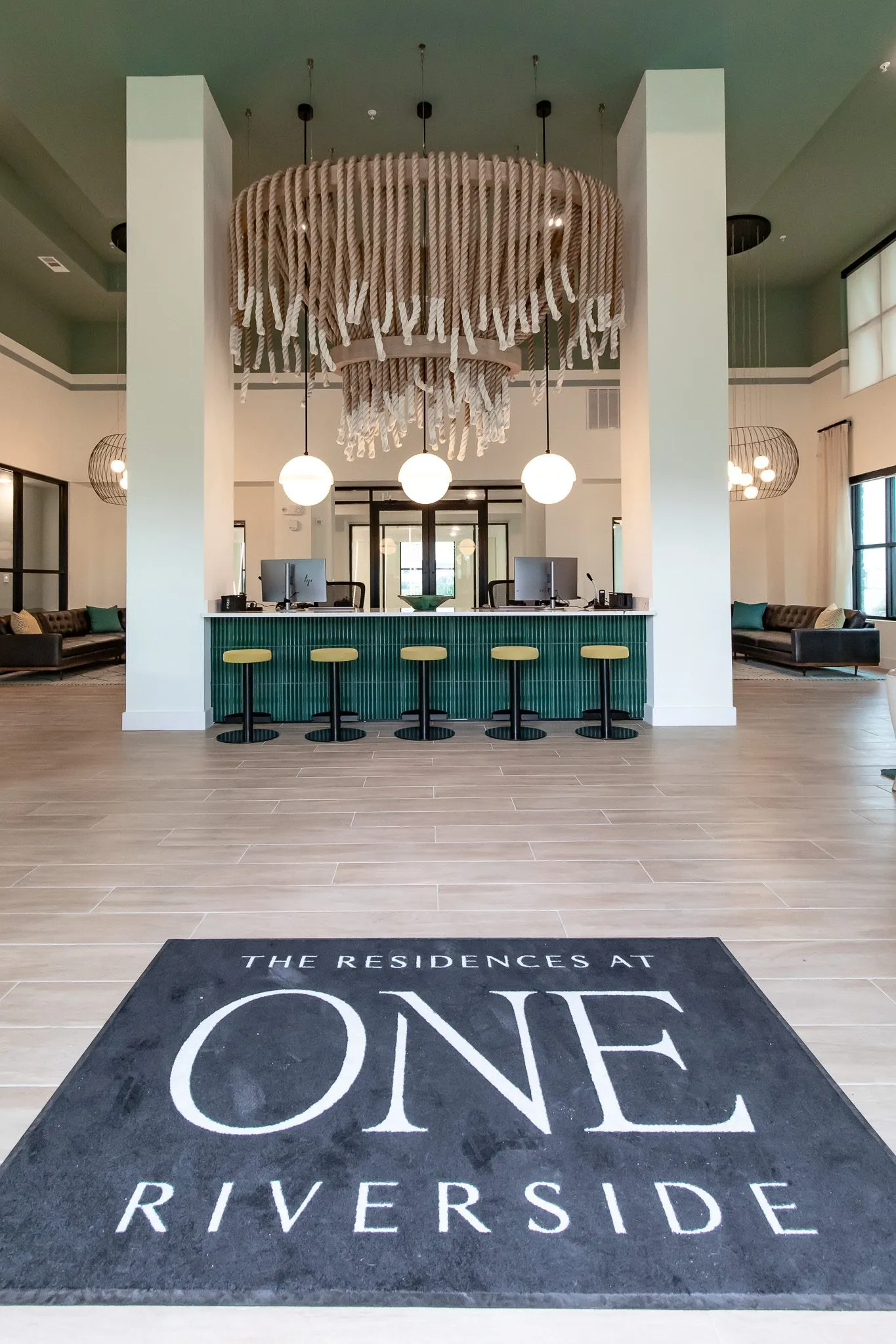 Multifamily amenity lobby from the logo entry mat to the teal tiled leasing desk and yellow stools under the rope chandelier