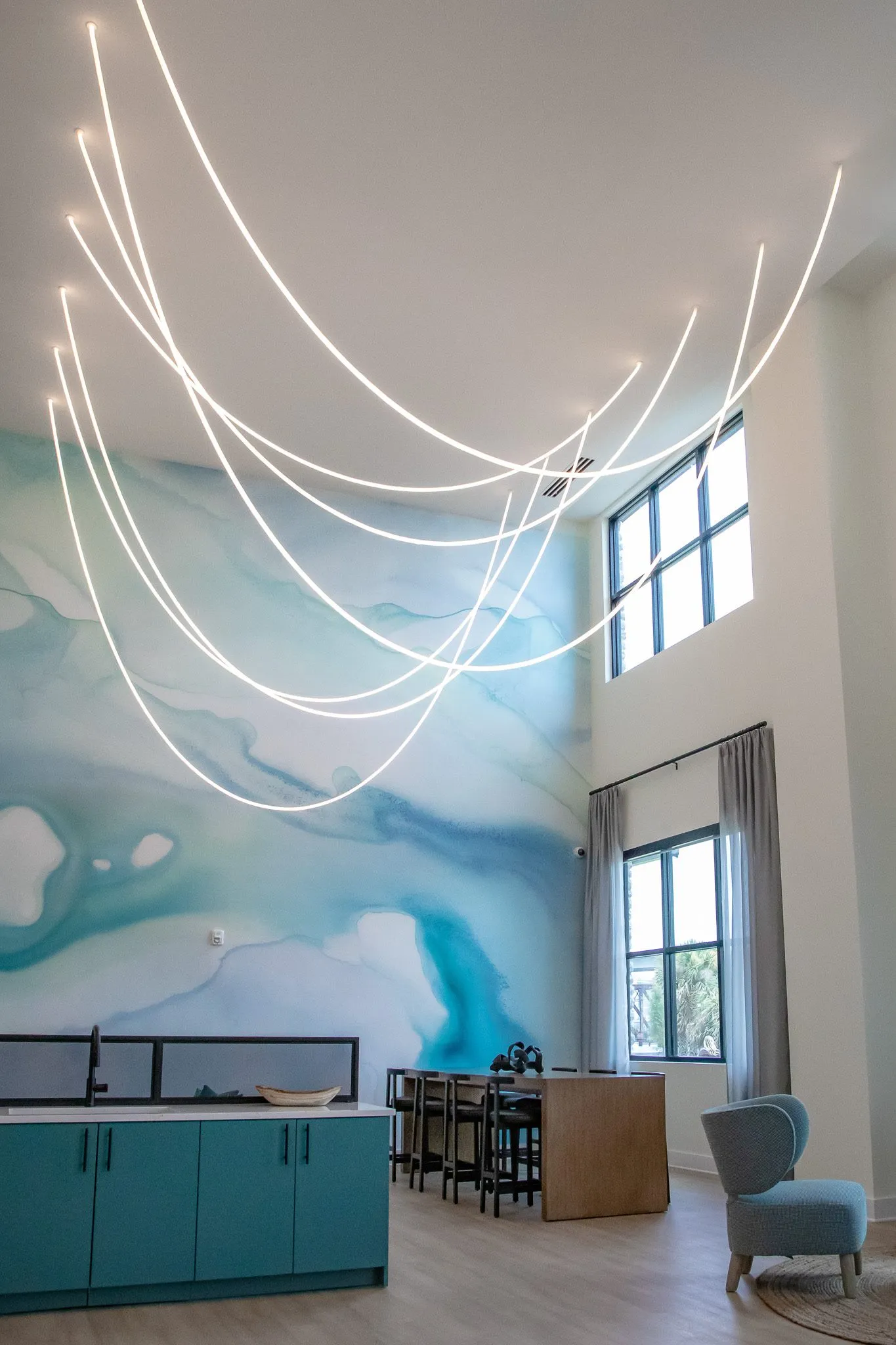 Multifamily amenity two storey lounge with looping light strands before a blue watercolor mural and teal cabinets