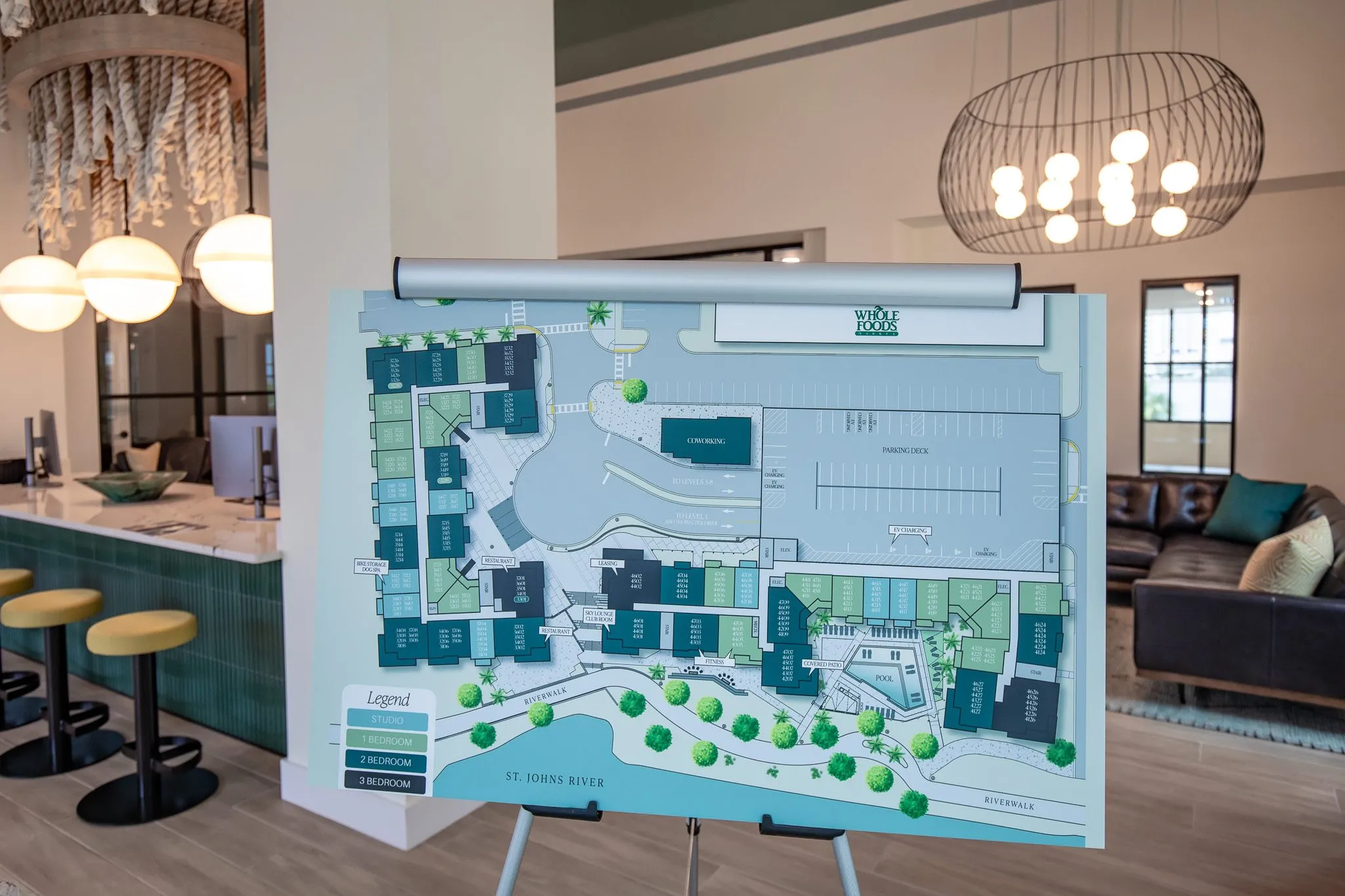 Multifamily amenity lobby with a site plan on an easel, the leasing desk with yellow stools and a wire globe chandelier
