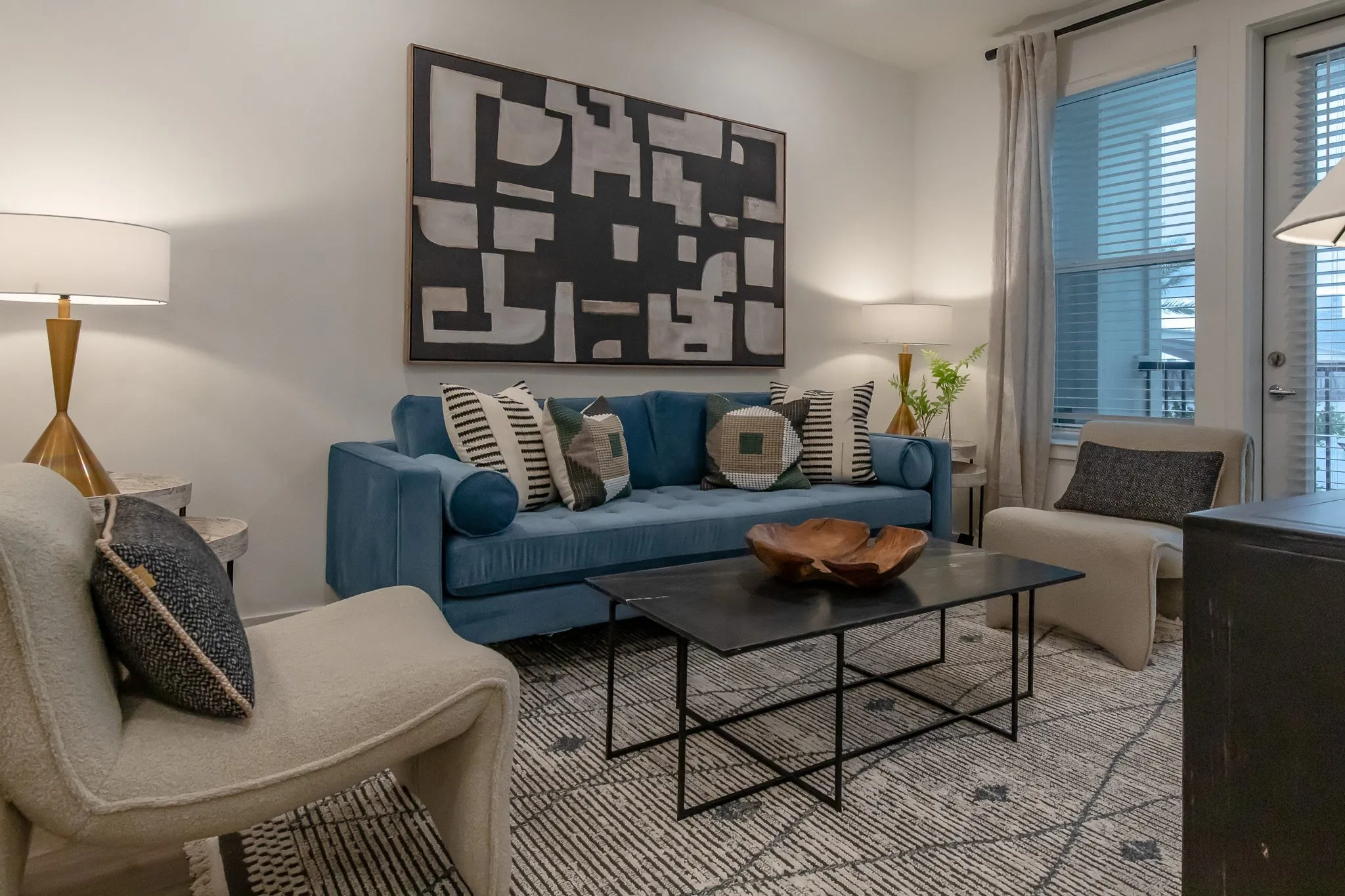 Multifamily model apartment living room with a blue velvet sofa and black metal coffee table below a black and white abstract