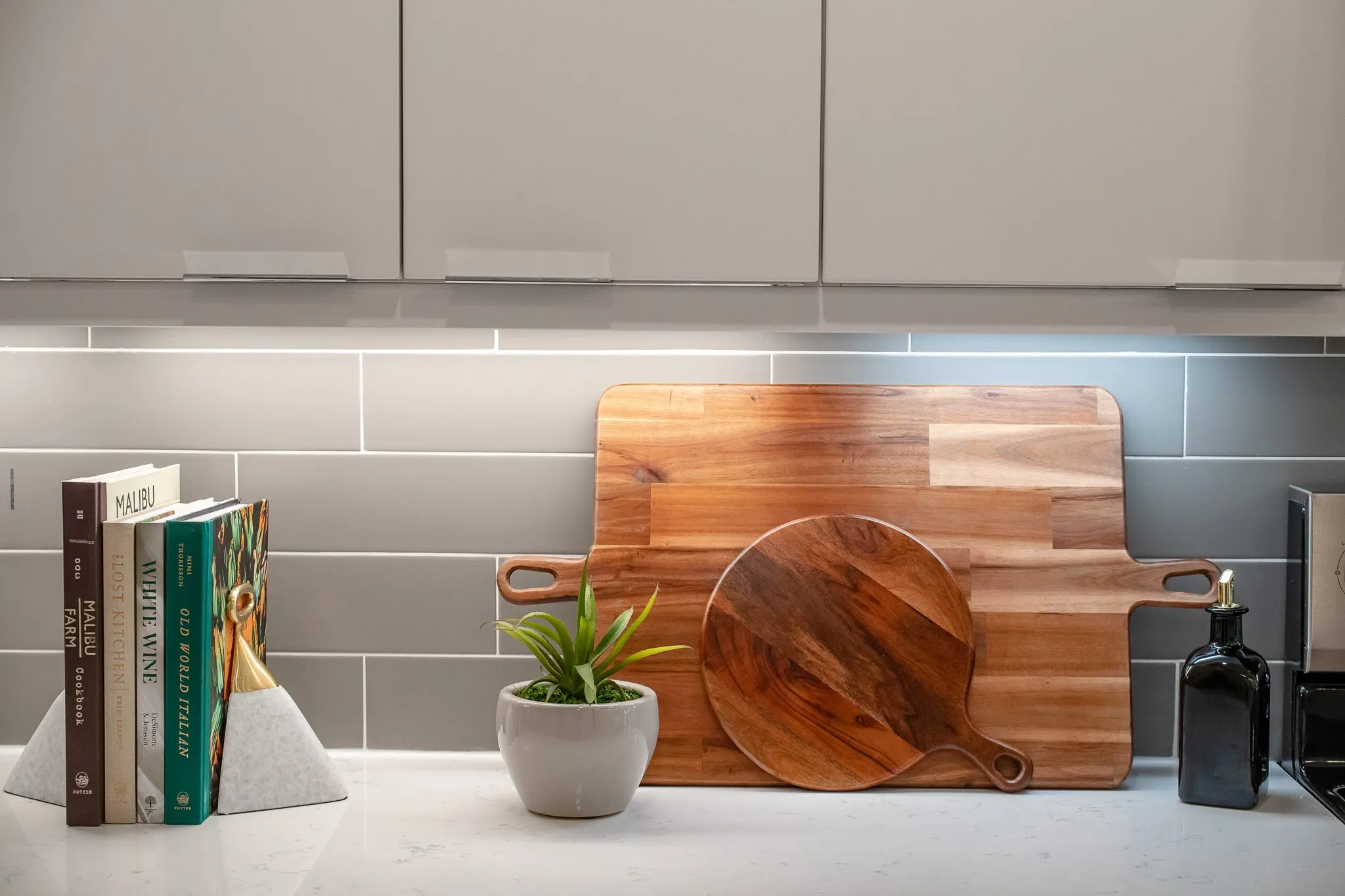 Multifamily kitchen counter with cookbooks, wood cutting boards and a succulent against grey tile