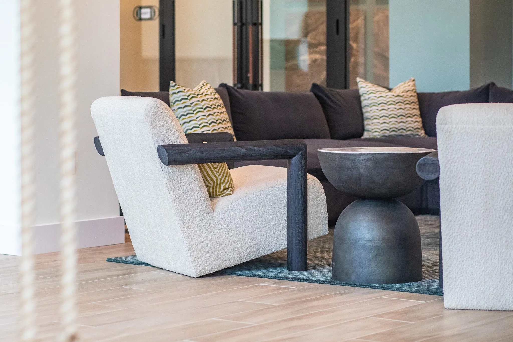 Multifamily interior detail: white boucle lounge chairs with dark wood arms around an hourglass table, a charcoal sectional