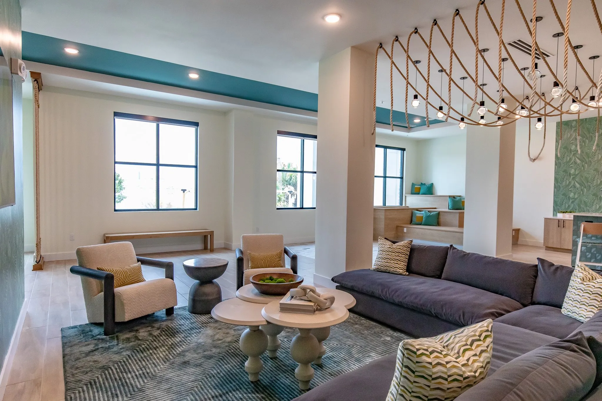 Multifamily amenity lounge with a charcoal sectional, boucle chairs and grey nesting tables under draped rope lights