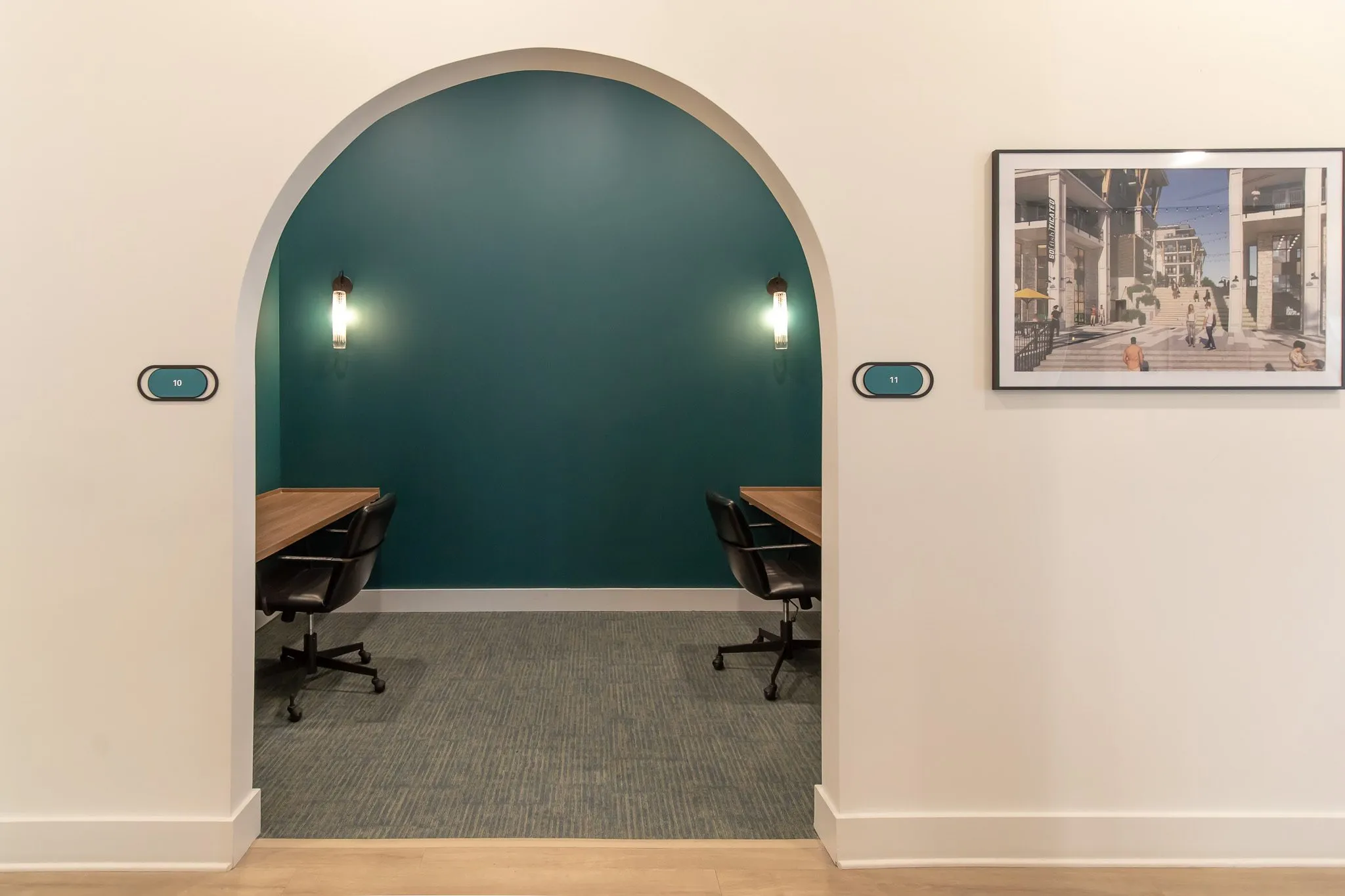 Multifamily amenity study room through a teal arched opening, desks, black chairs and sconces, a street photograph beside