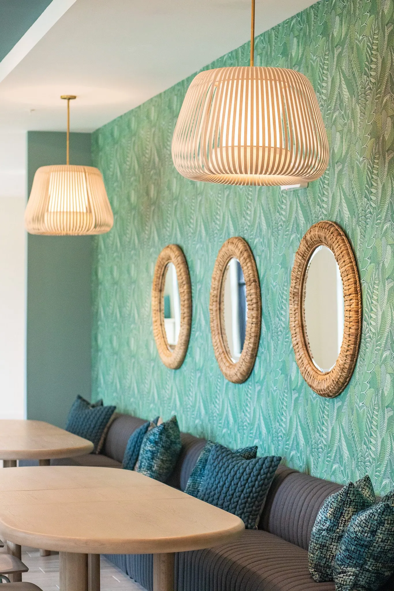 Multifamily interior detail: slatted pendants and three round rattan mirrors over a navy banquette with teal pillows