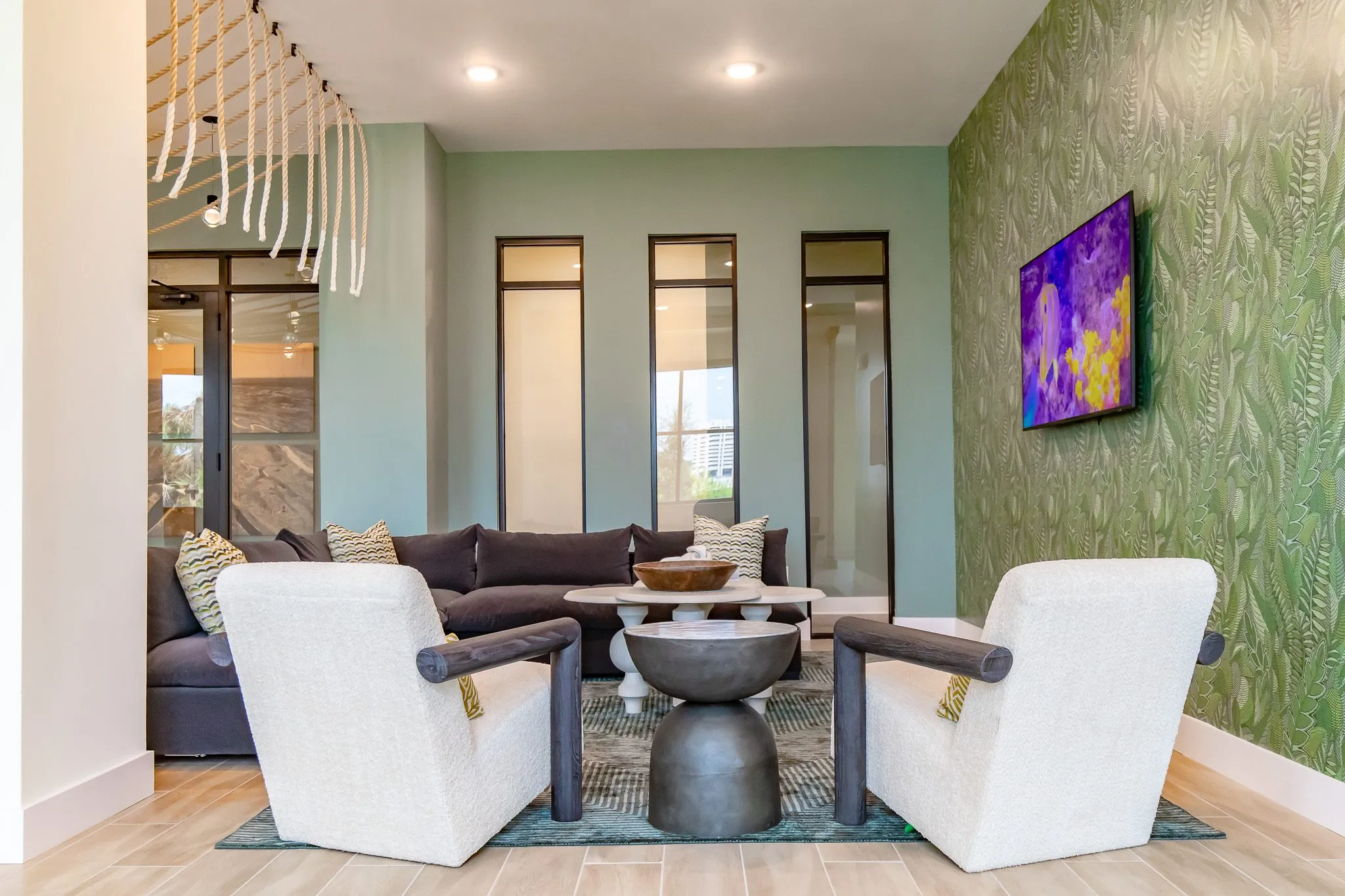 Multifamily amenity lounge with two white boucle chairs and an hourglass table before a charcoal sectional and leaf wallpaper