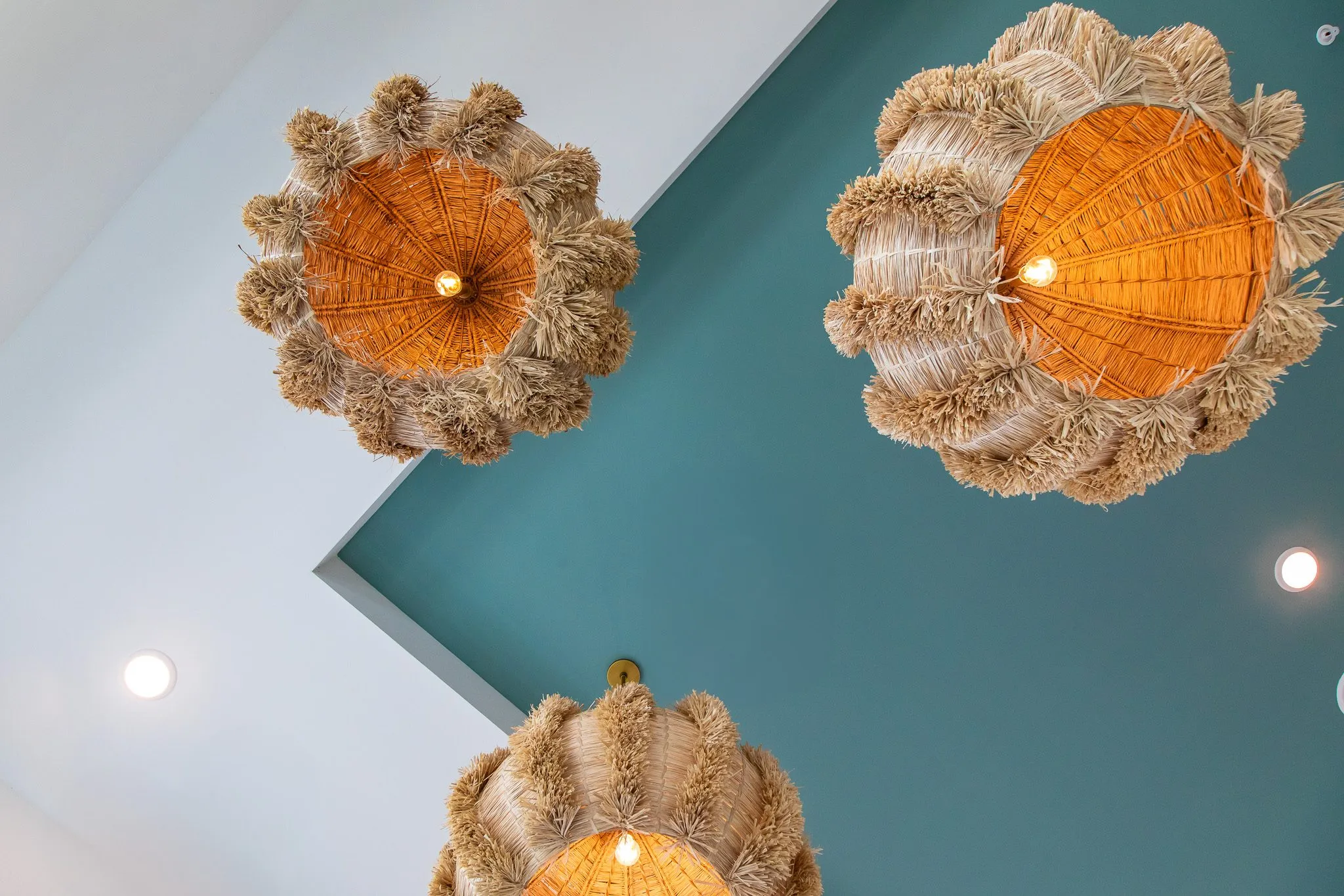 Multifamily interior detail: looking up at fringed rattan pendants against a white and teal ceiling